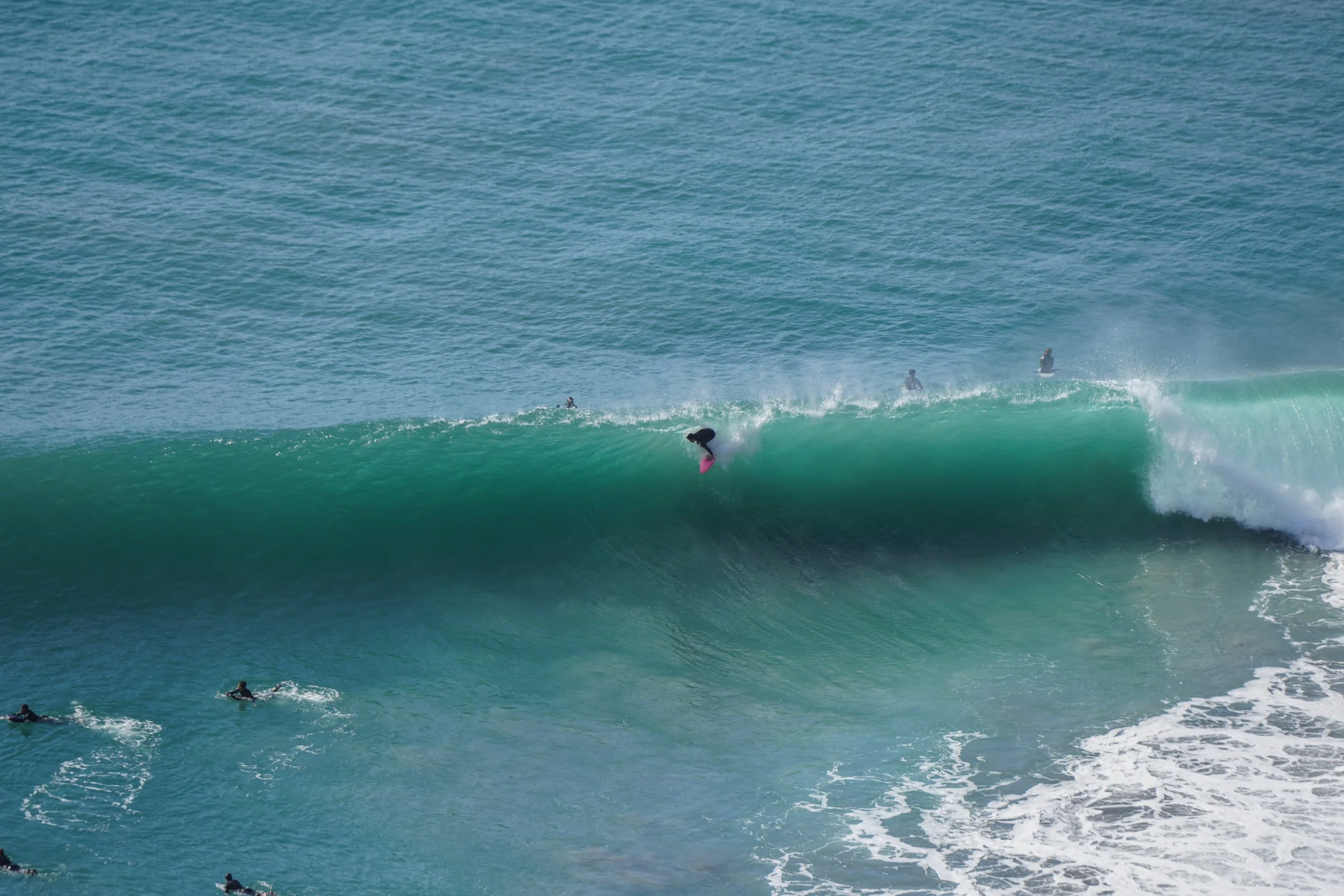 Surfer riding a large wave while others wait in the water.