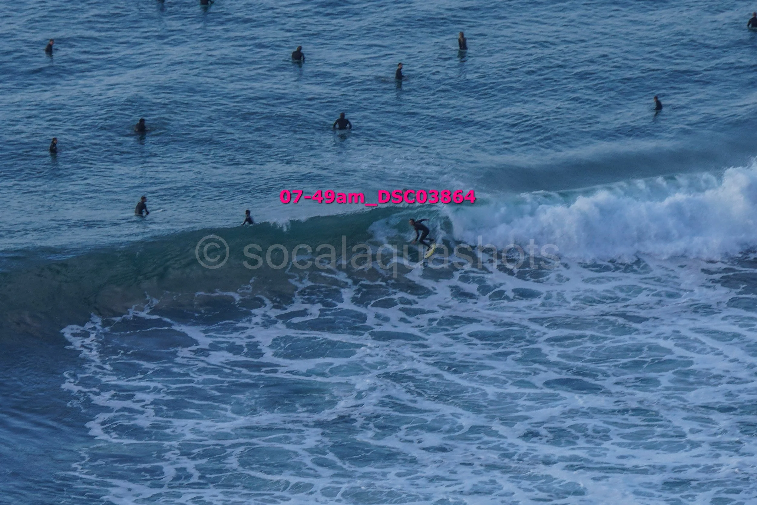 A person surfing on a wave in the ocean with multiple people swimming and floating in the background.