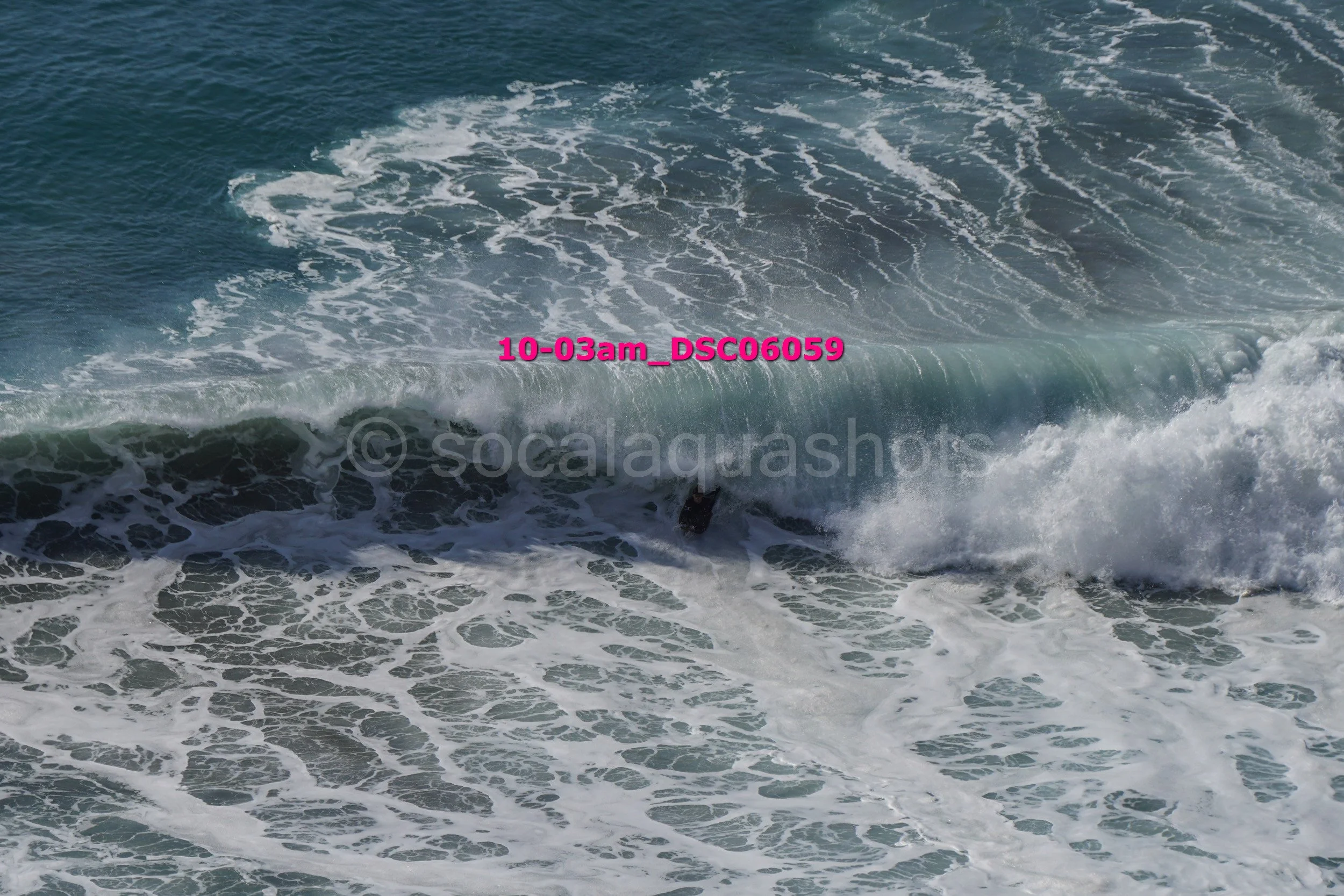 Orange surfboard in rough ocean waves with white foam, viewed from above.