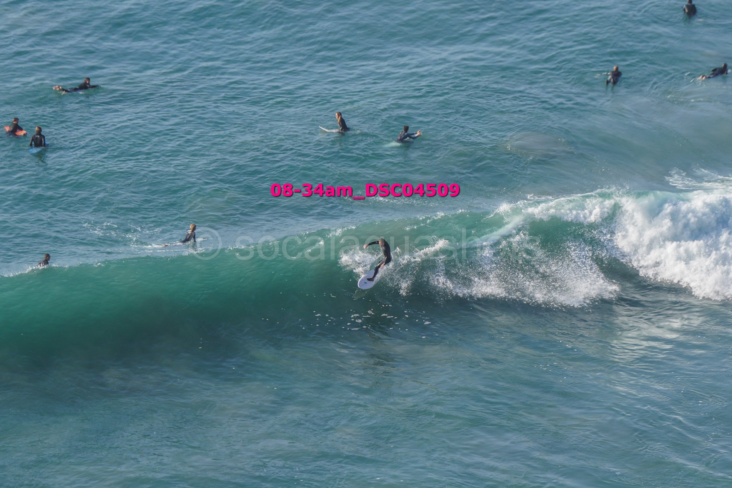 A group of surfers waiting in the water, with one surfer riding a wave on a surfboard.