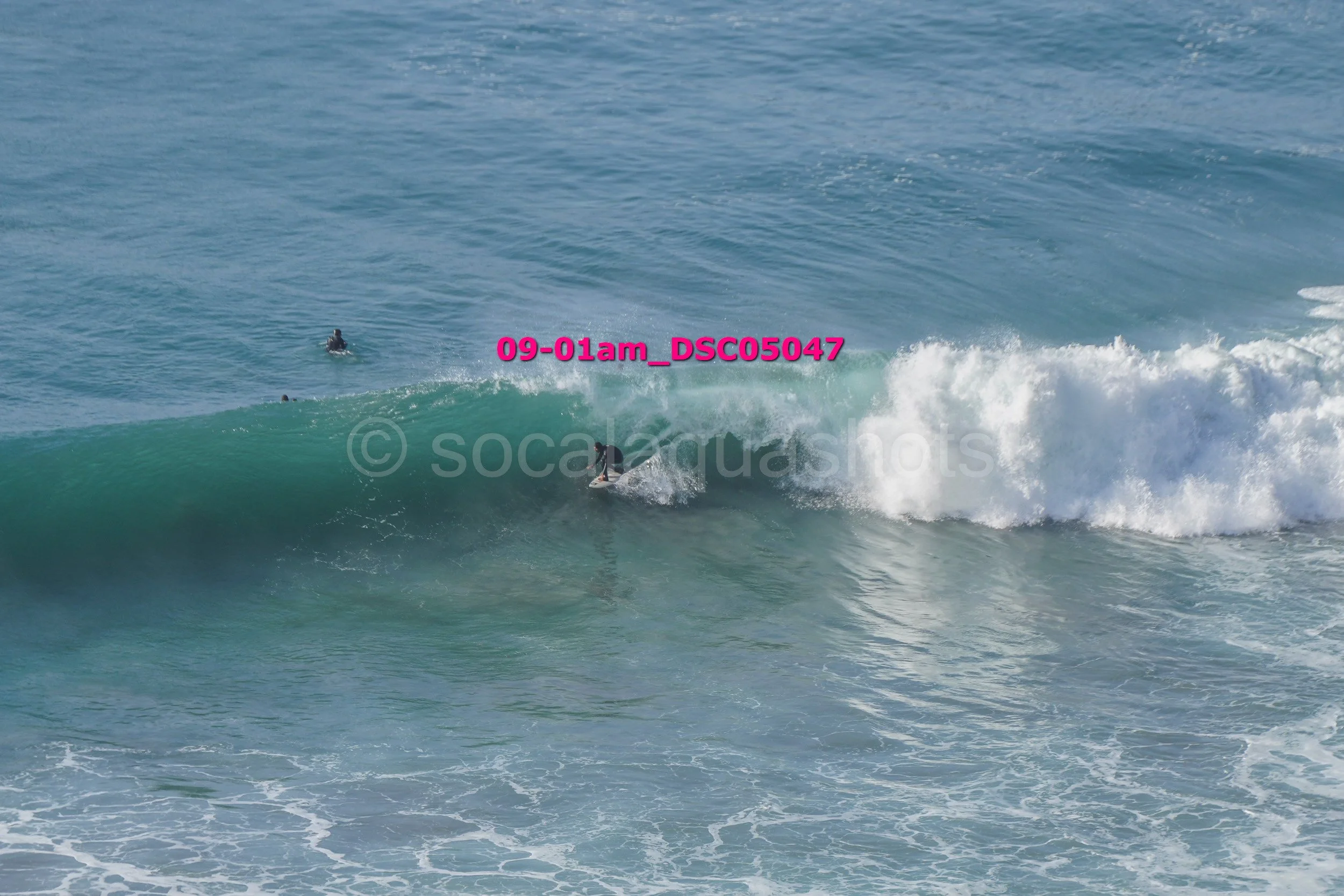 Surfer riding a wave in the ocean with two other surfers in the background