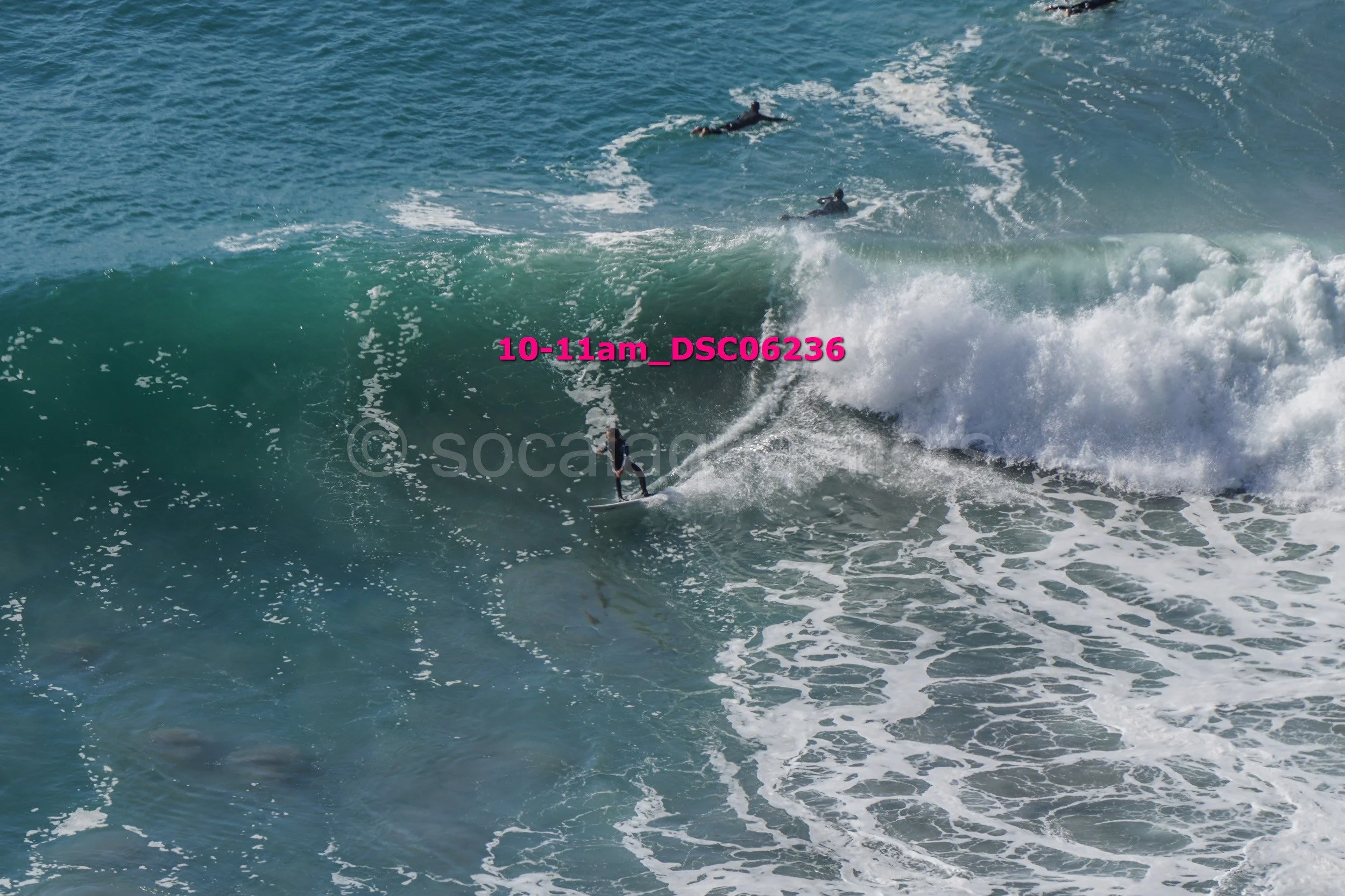 Surfers riding large ocean waves with a bright blue water background.