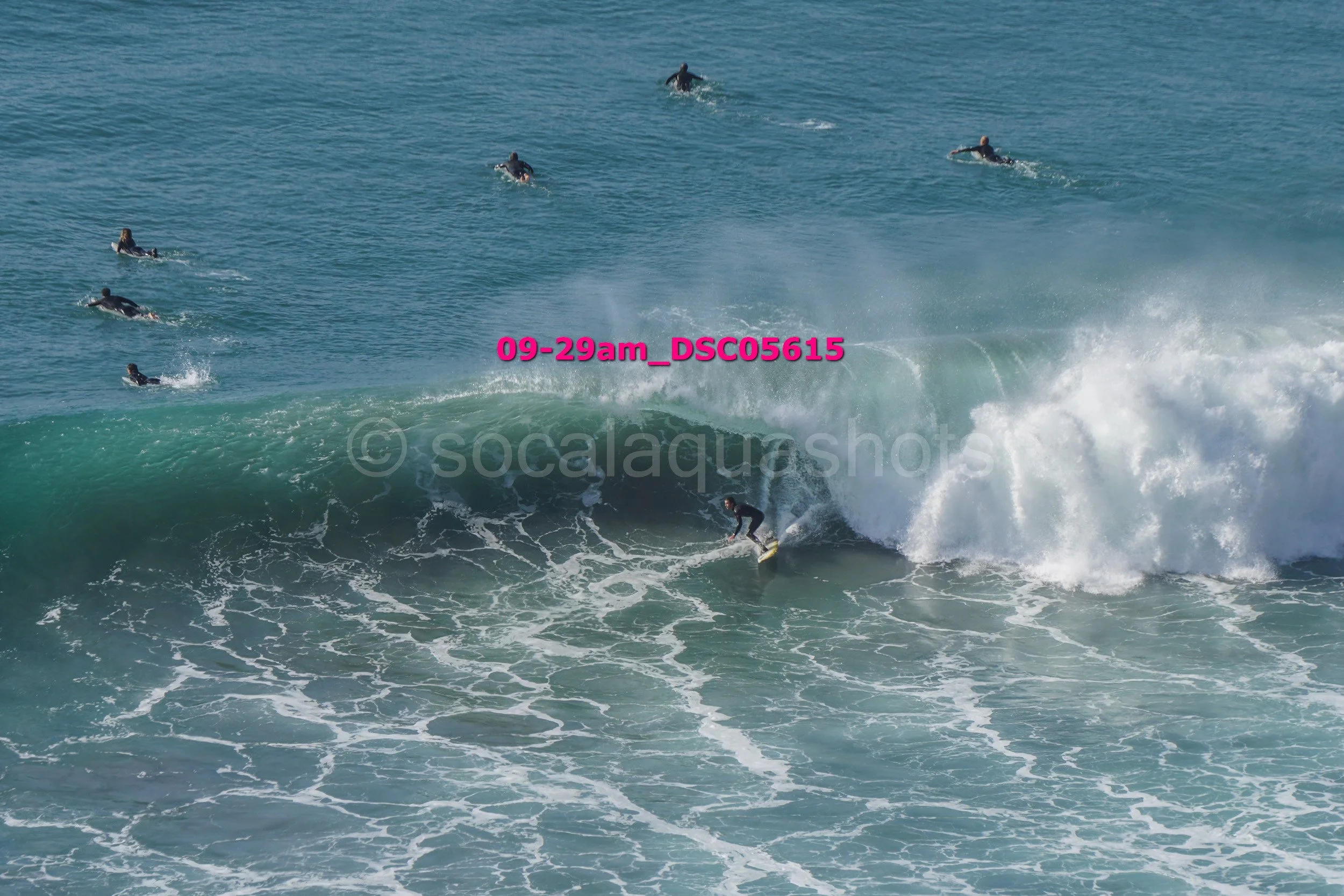 A person surfing on a large wave with several surfers in the background in the ocean.