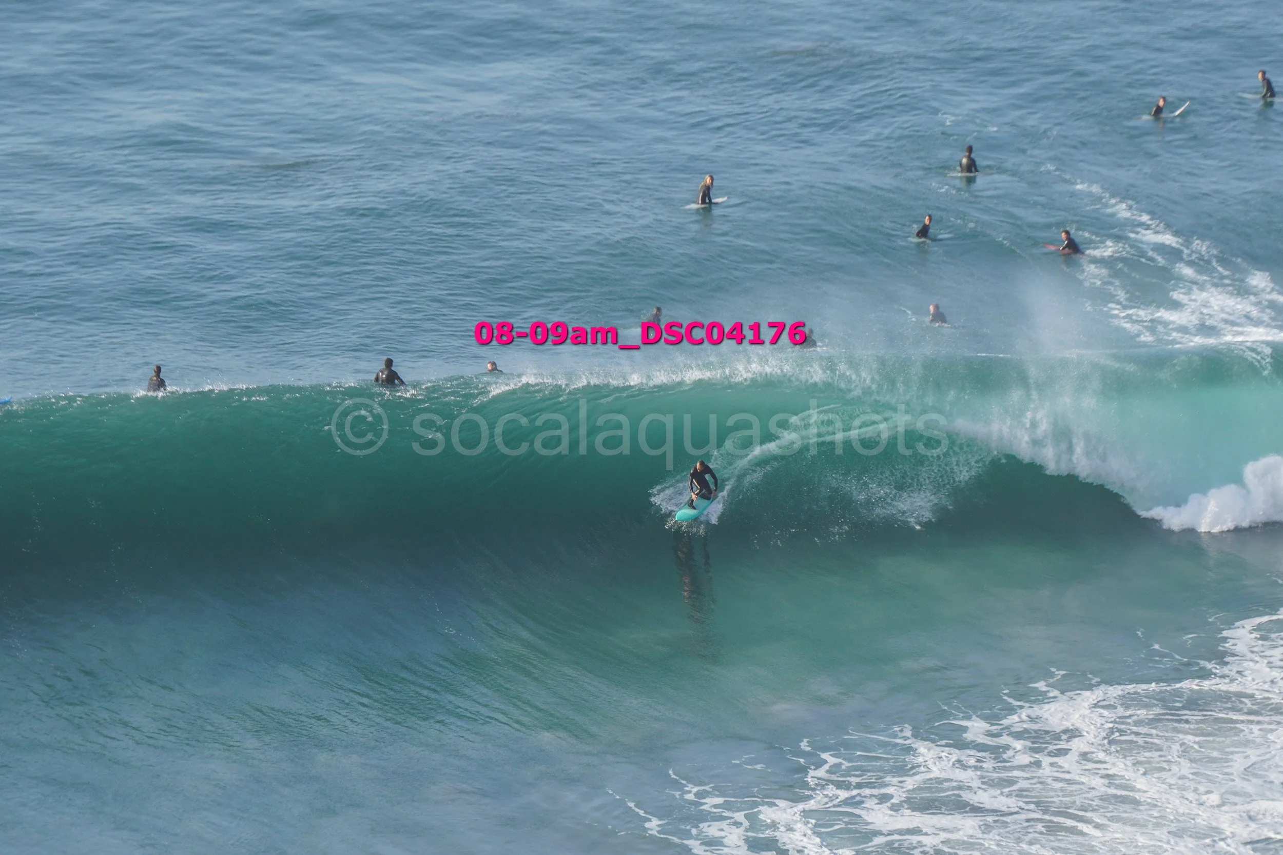 A surfer riding a wave with multiple surfers in the water watching or waiting in the background.