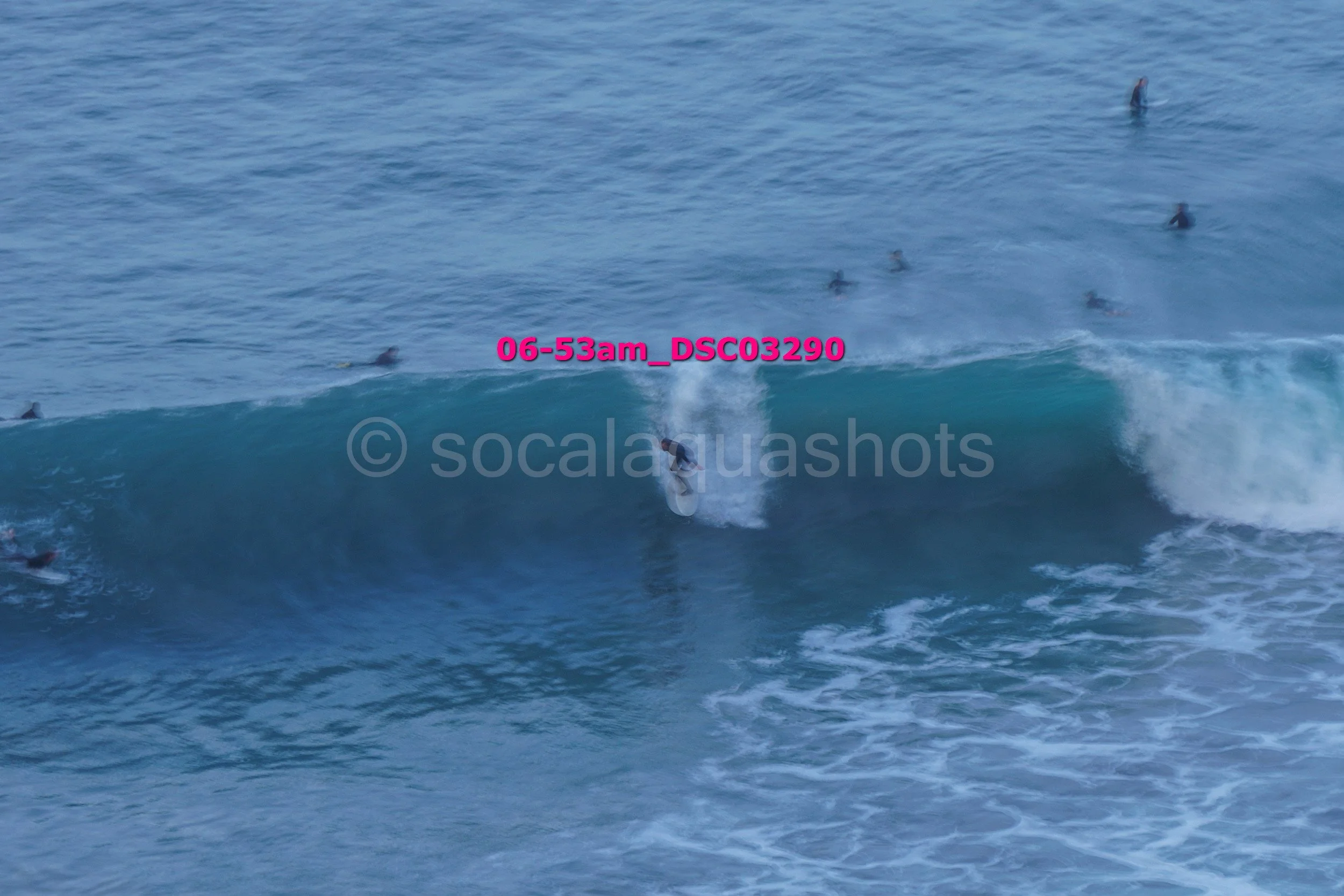 A person surfing on a wave in the ocean with several other surfers in the water nearby.