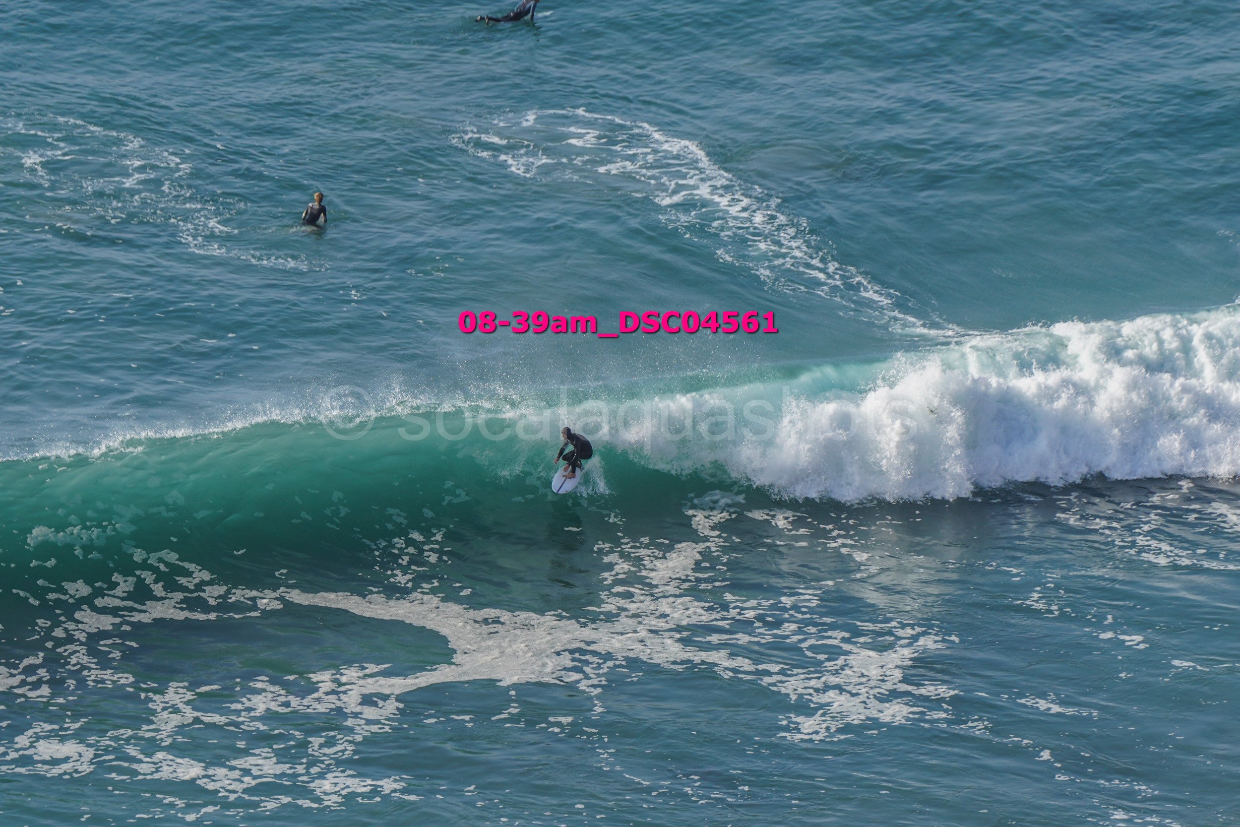 A person surfing on a wave in the ocean with two other surfers visible in the water in the background.