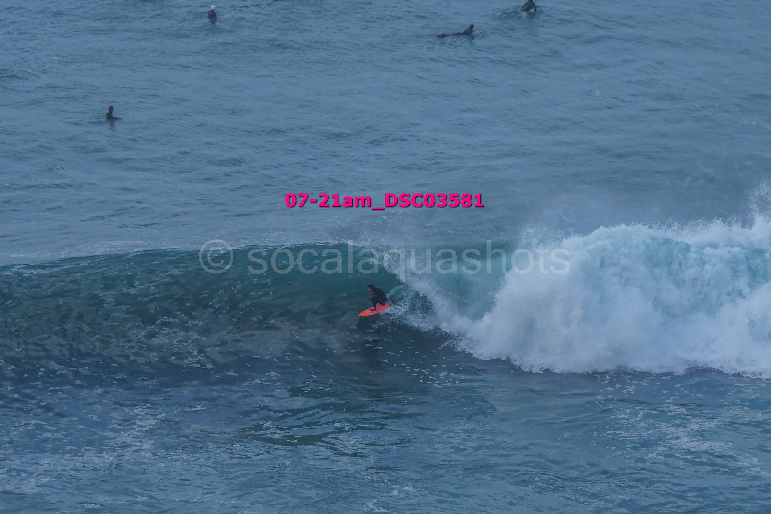 A person surfing on a wave in the ocean with several other surfers in the background.
