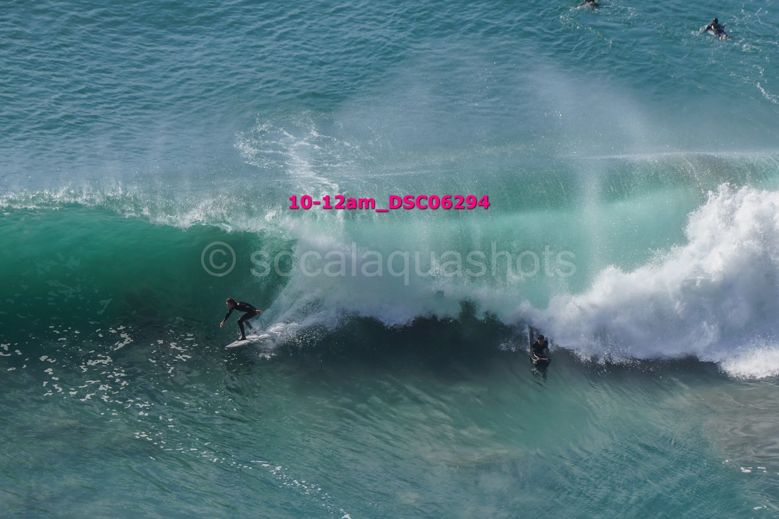 Surfer riding a large ocean wave with several other surfers in the water.
