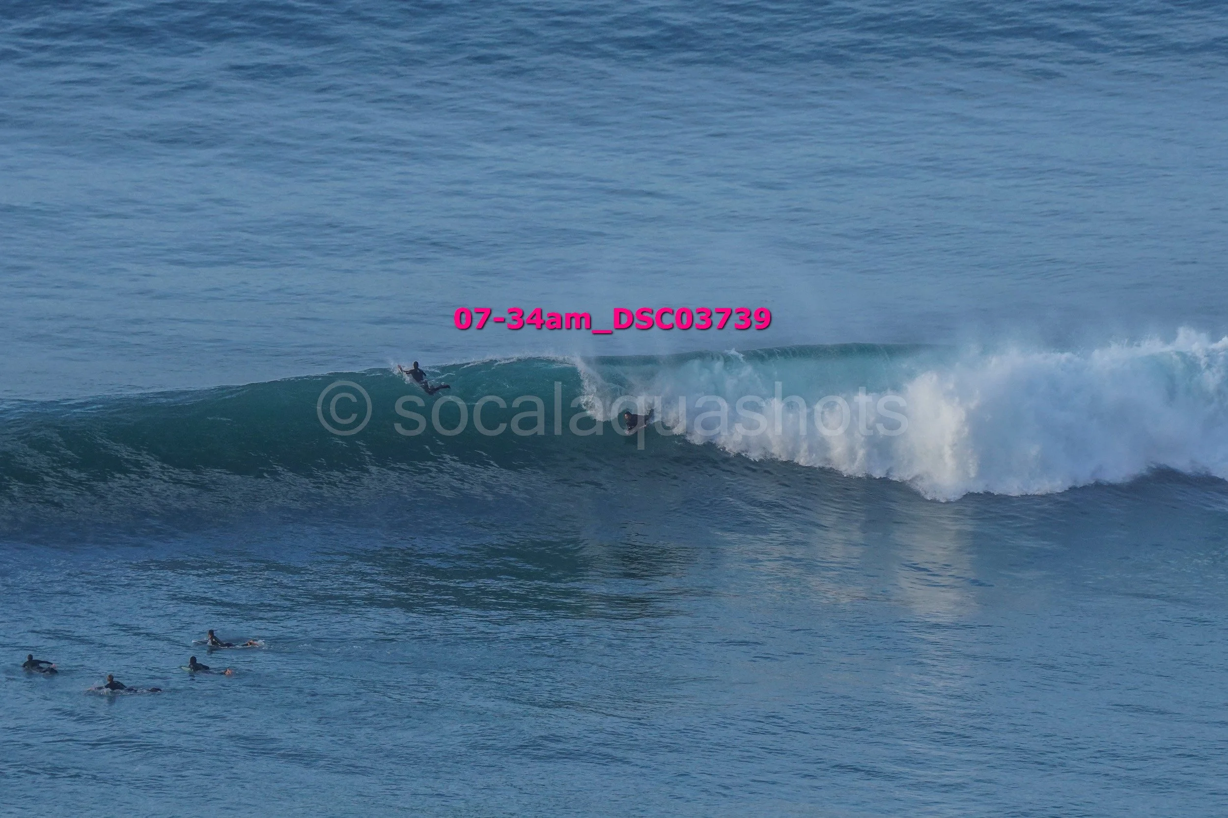 A surfer riding a wave in the ocean with a group of surfers waiting in the water nearby.