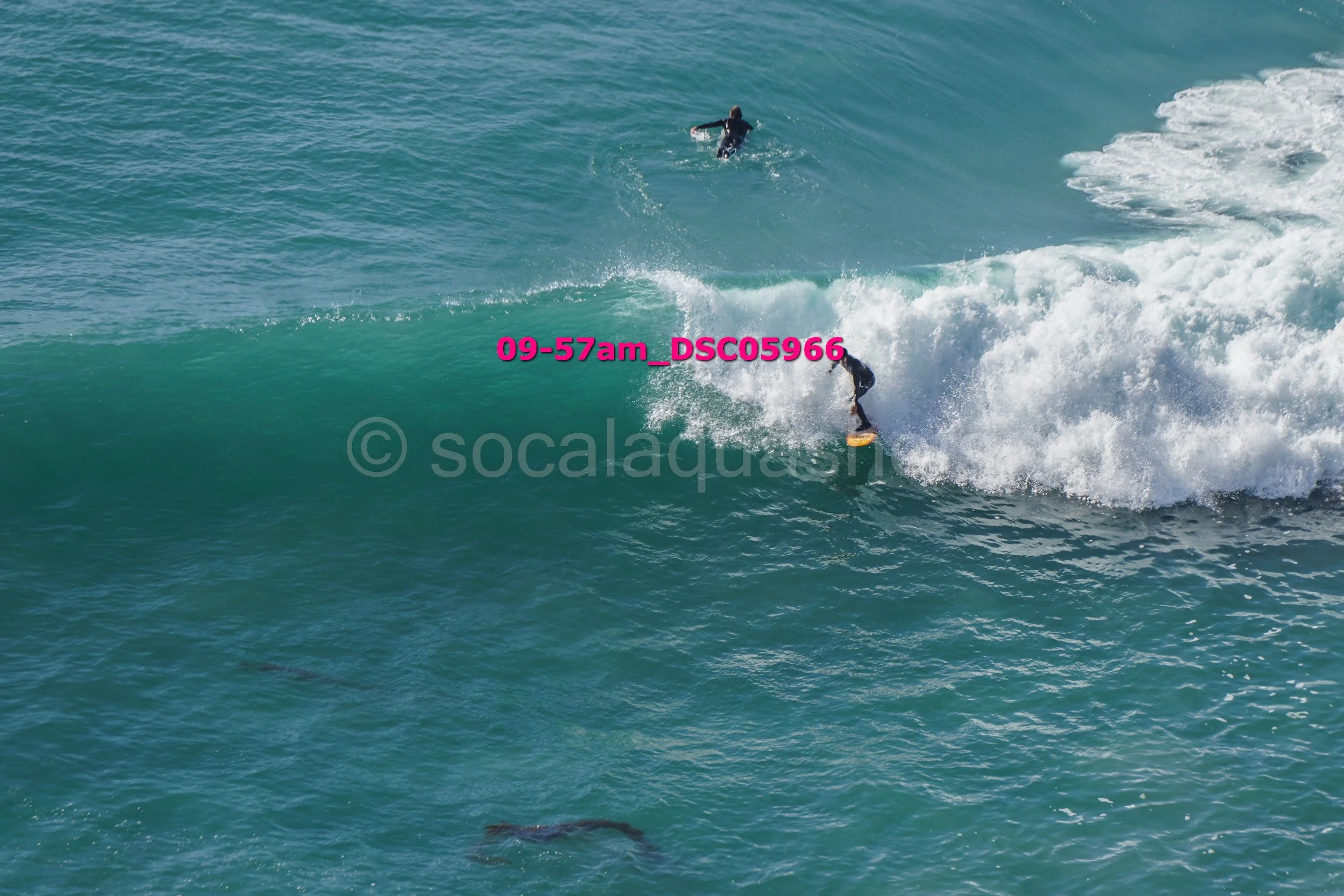 Two surfers riding a large wave in the ocean, one in the foreground and another in the background.