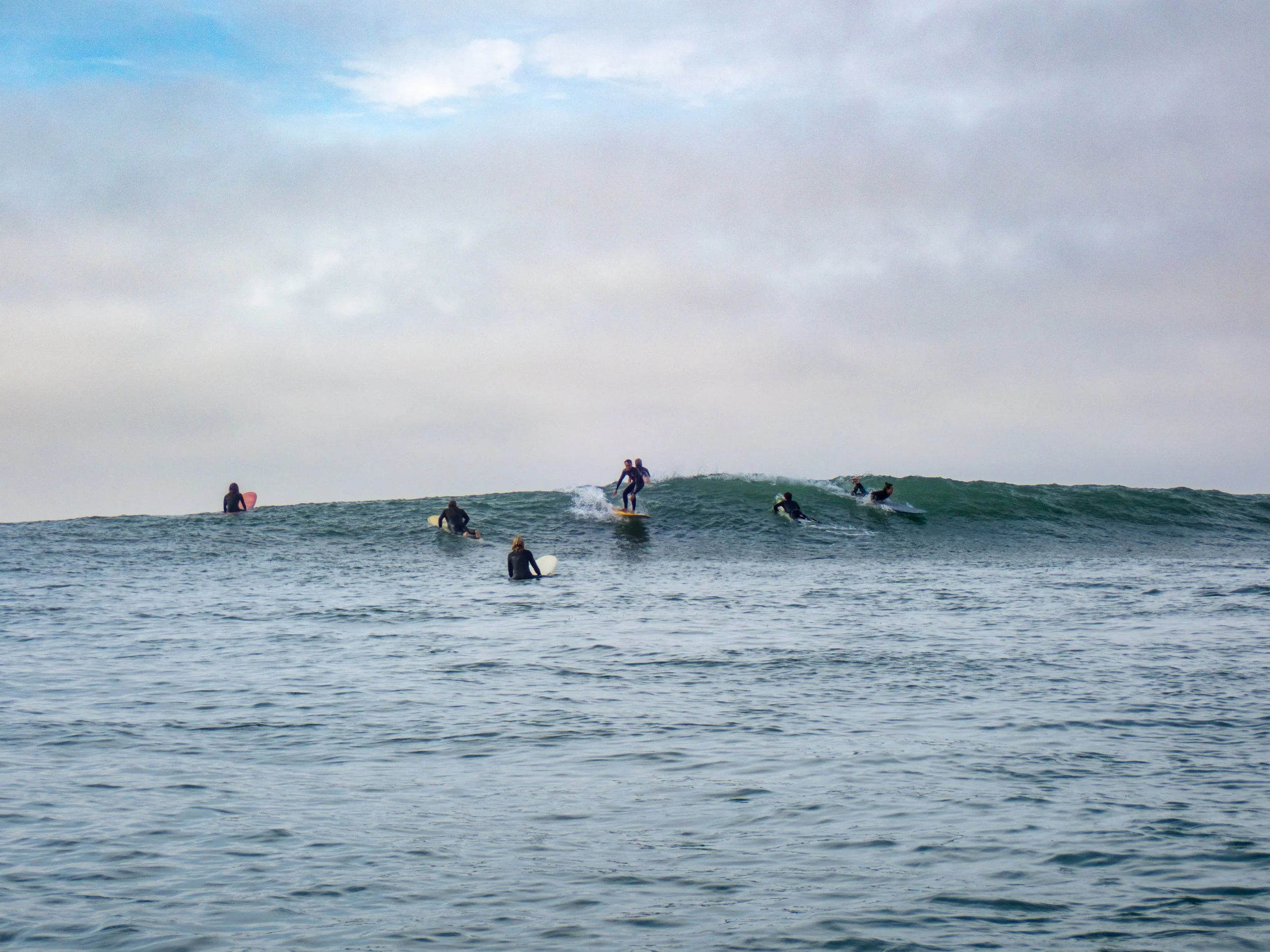 Several surfers riding and waiting for waves in the ocean under a cloudy sky.