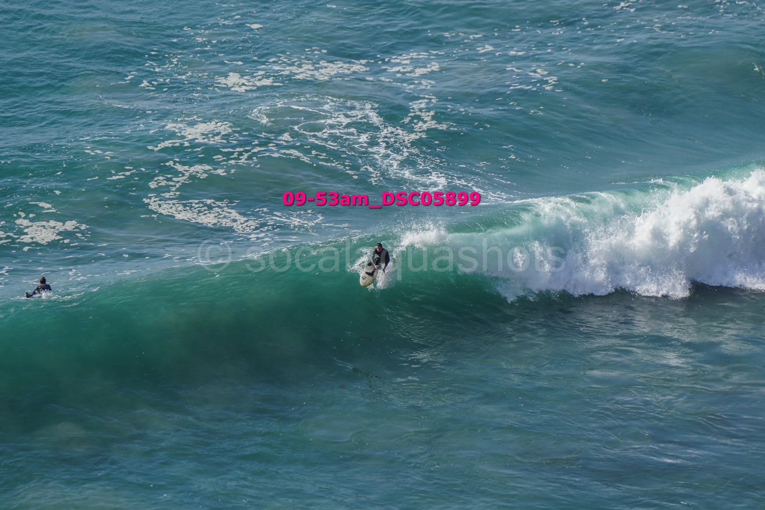 A person surfing on a wave in the ocean with another person in the water nearby.