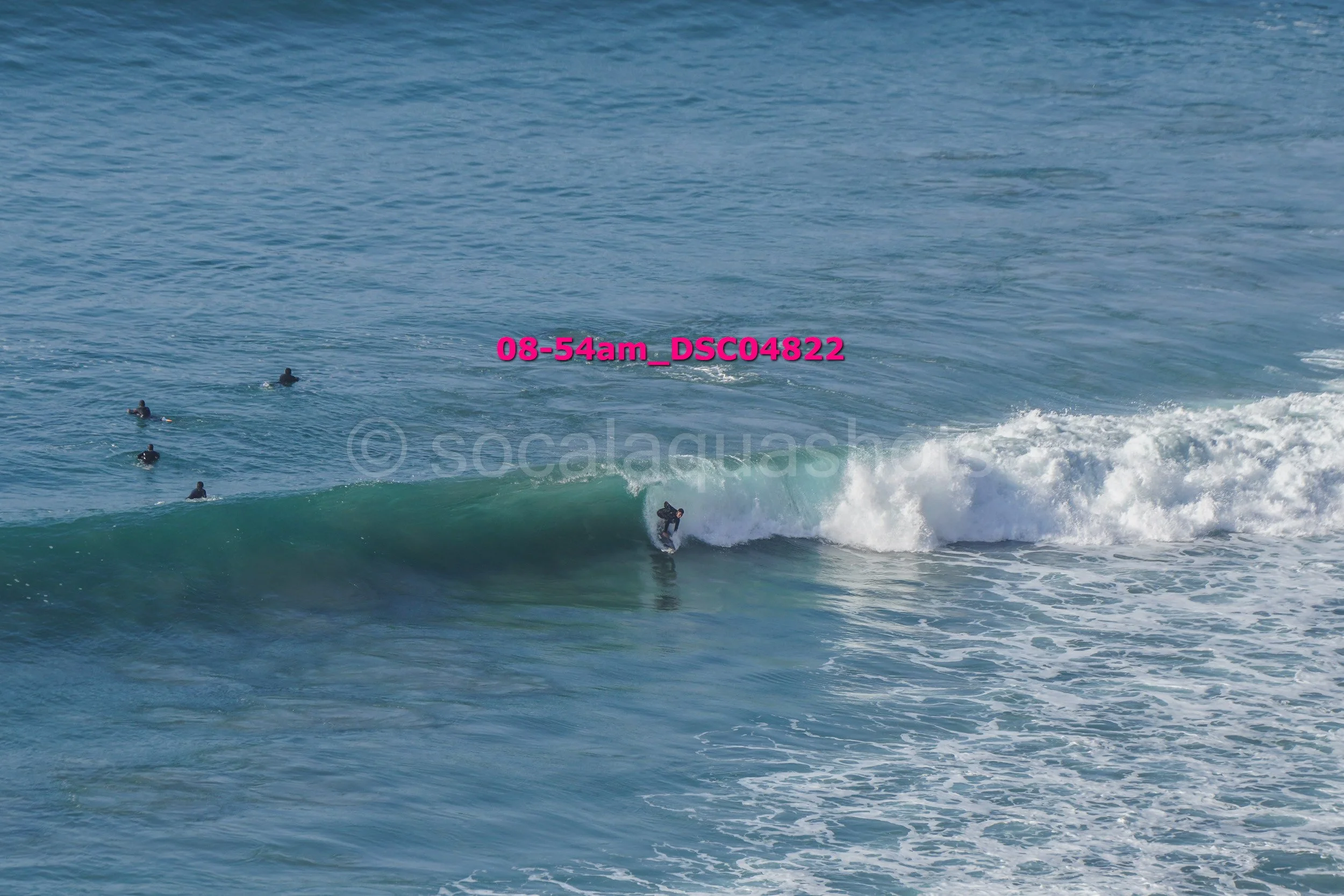 A surfer riding a wave with several surfers waiting in the water nearby.