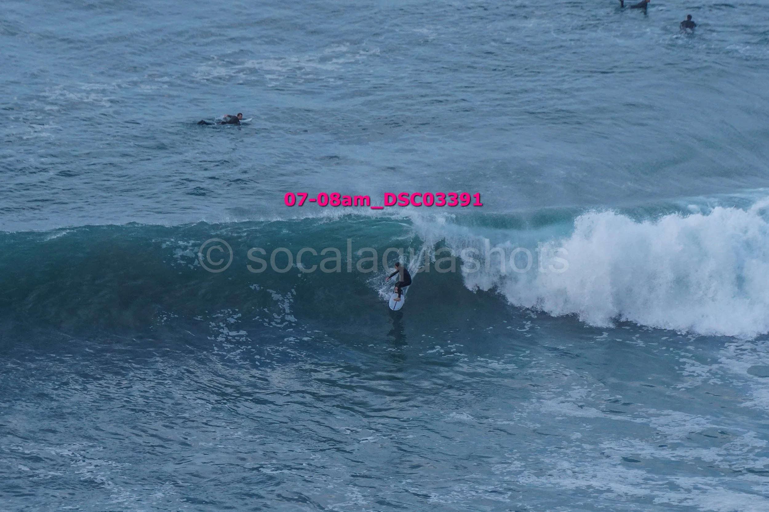 Surfer riding a wave in the ocean with several other surfers in the water in the background.
