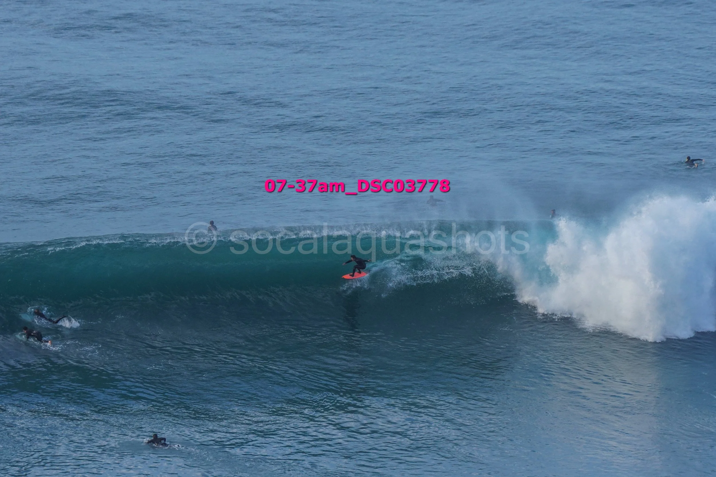 A person surfing on a wave with several other surfers in the water around them.