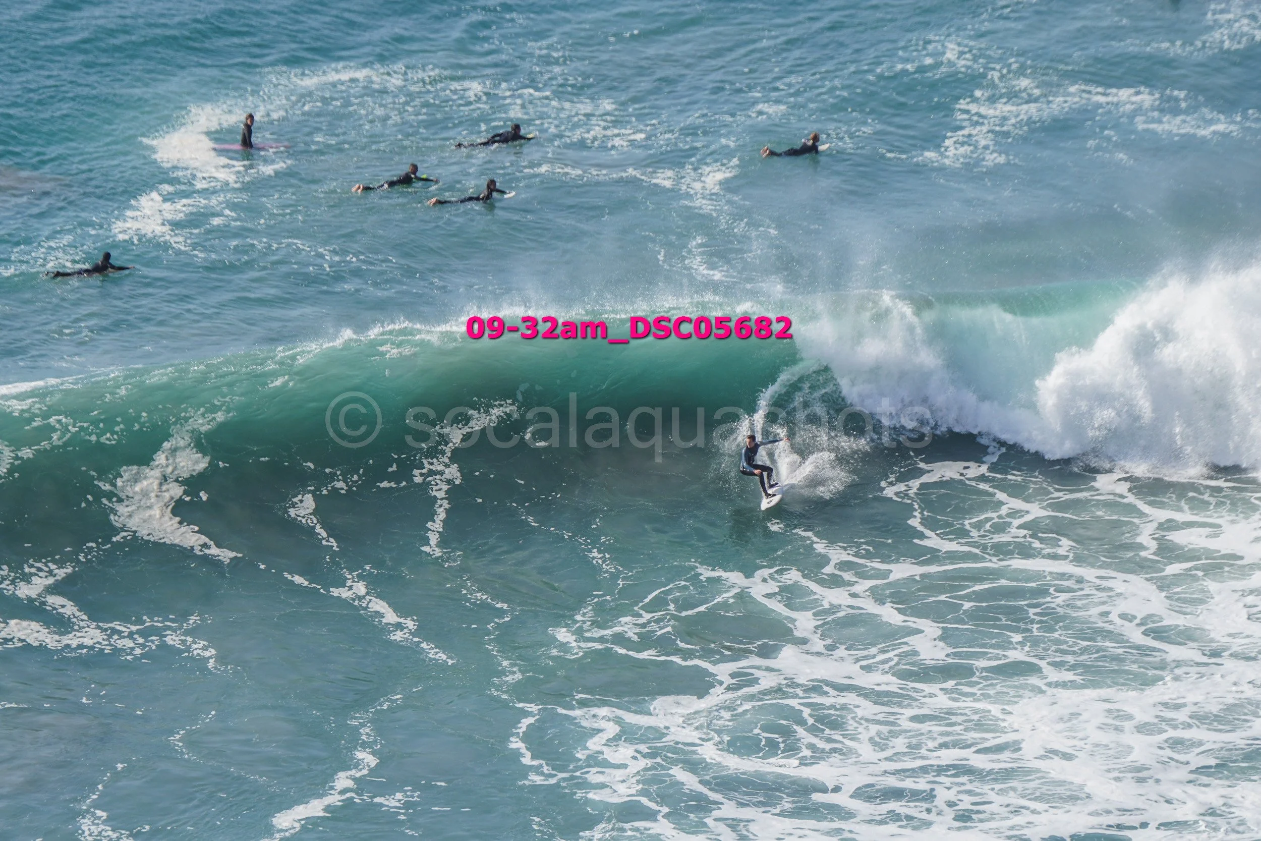 Surfer riding a wave with multiple surfers in the background in the ocean.