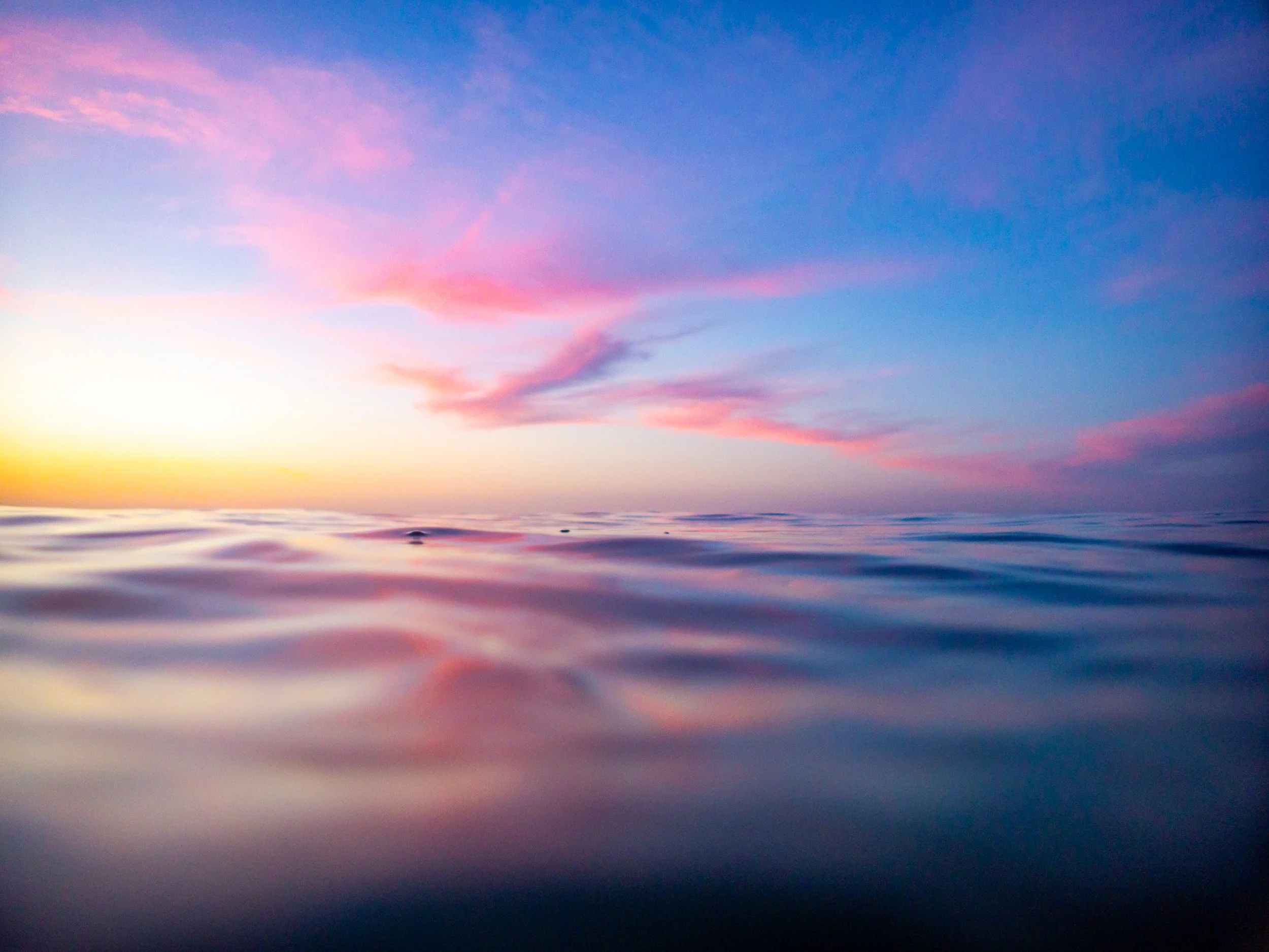 Calm ocean surface at sunset with pink and blue sky.