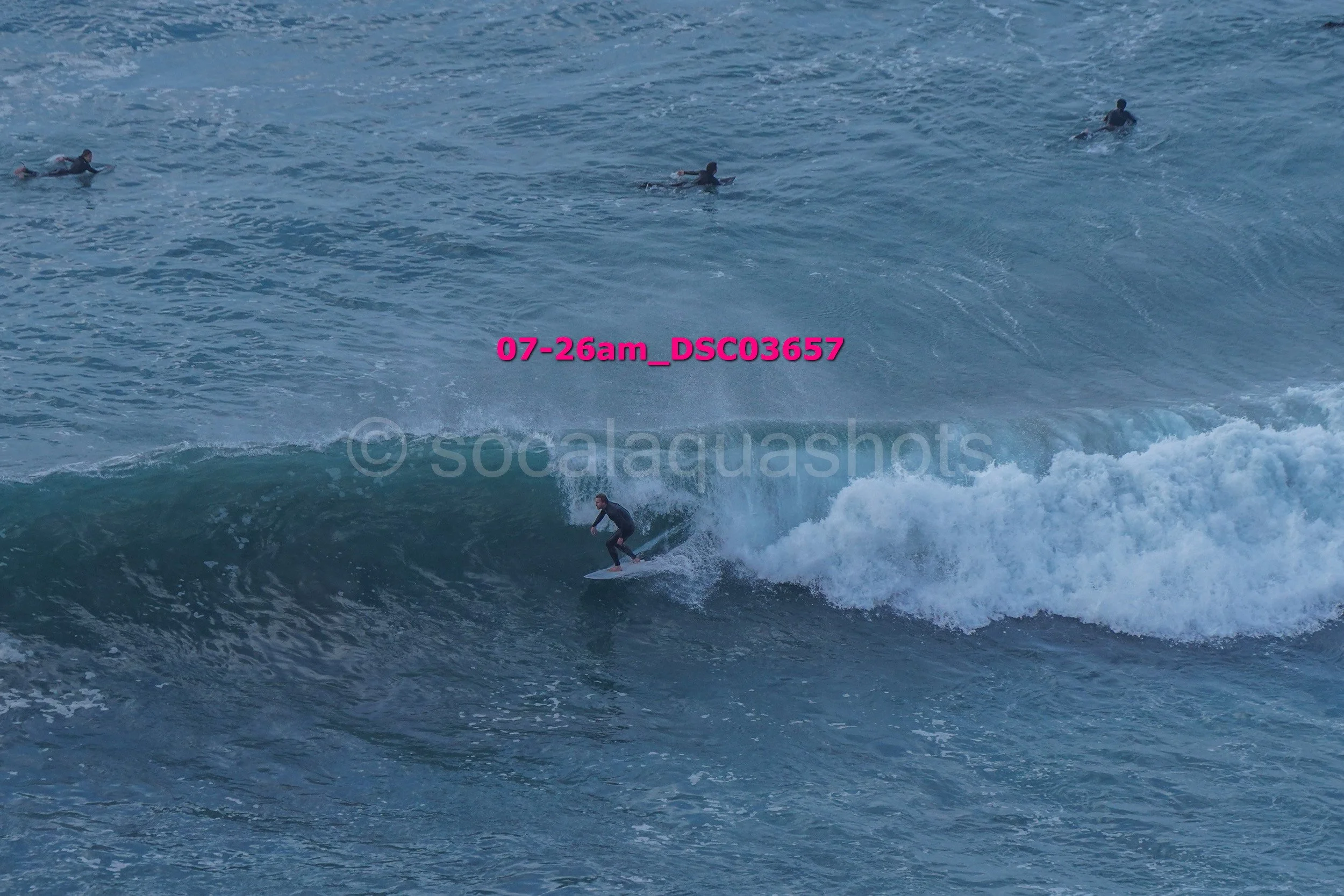 A person surfing on a wave in the ocean with three other surfers swimming in the background.
