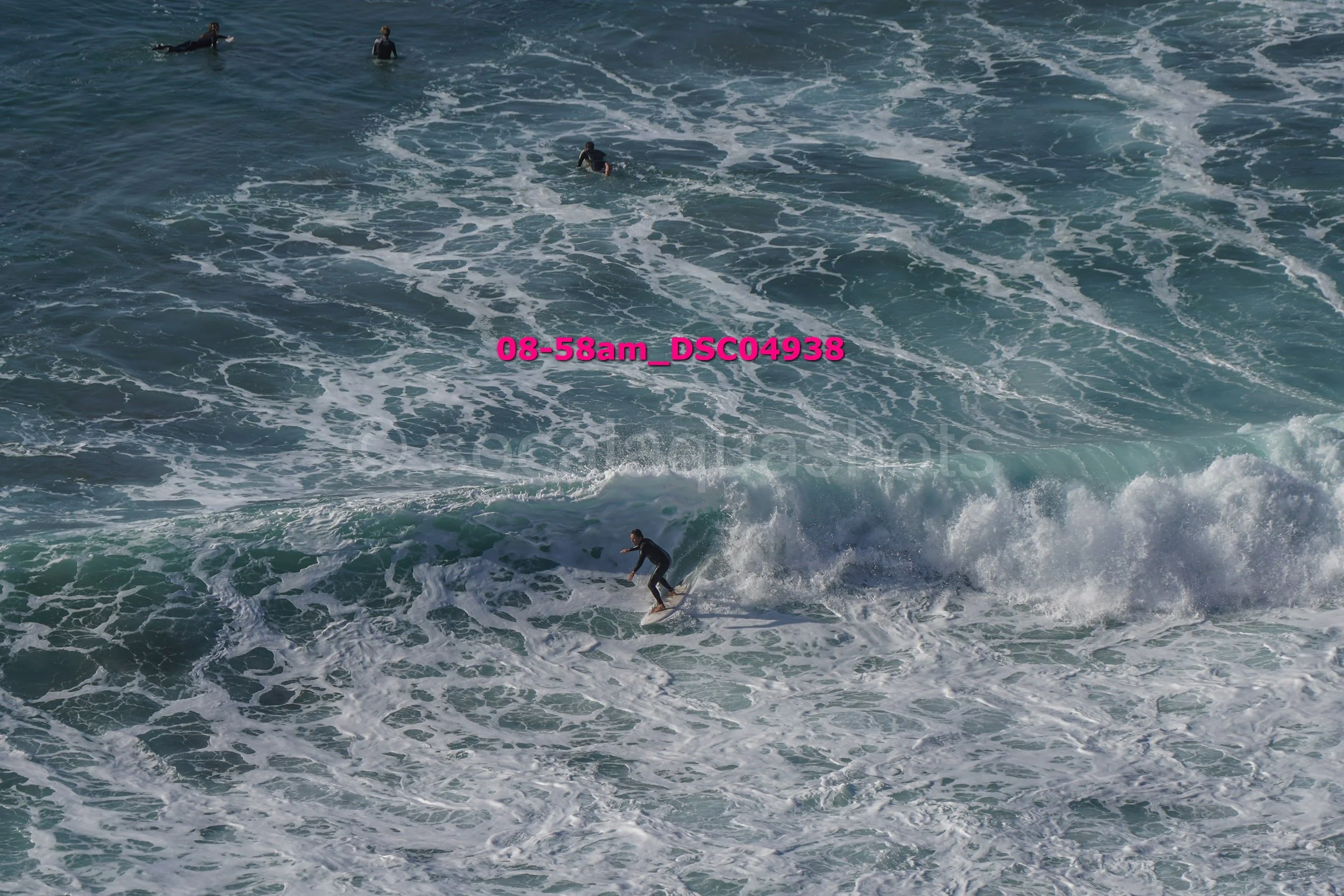 A person surfing on a wave in the ocean with several people swimming or floating nearby.