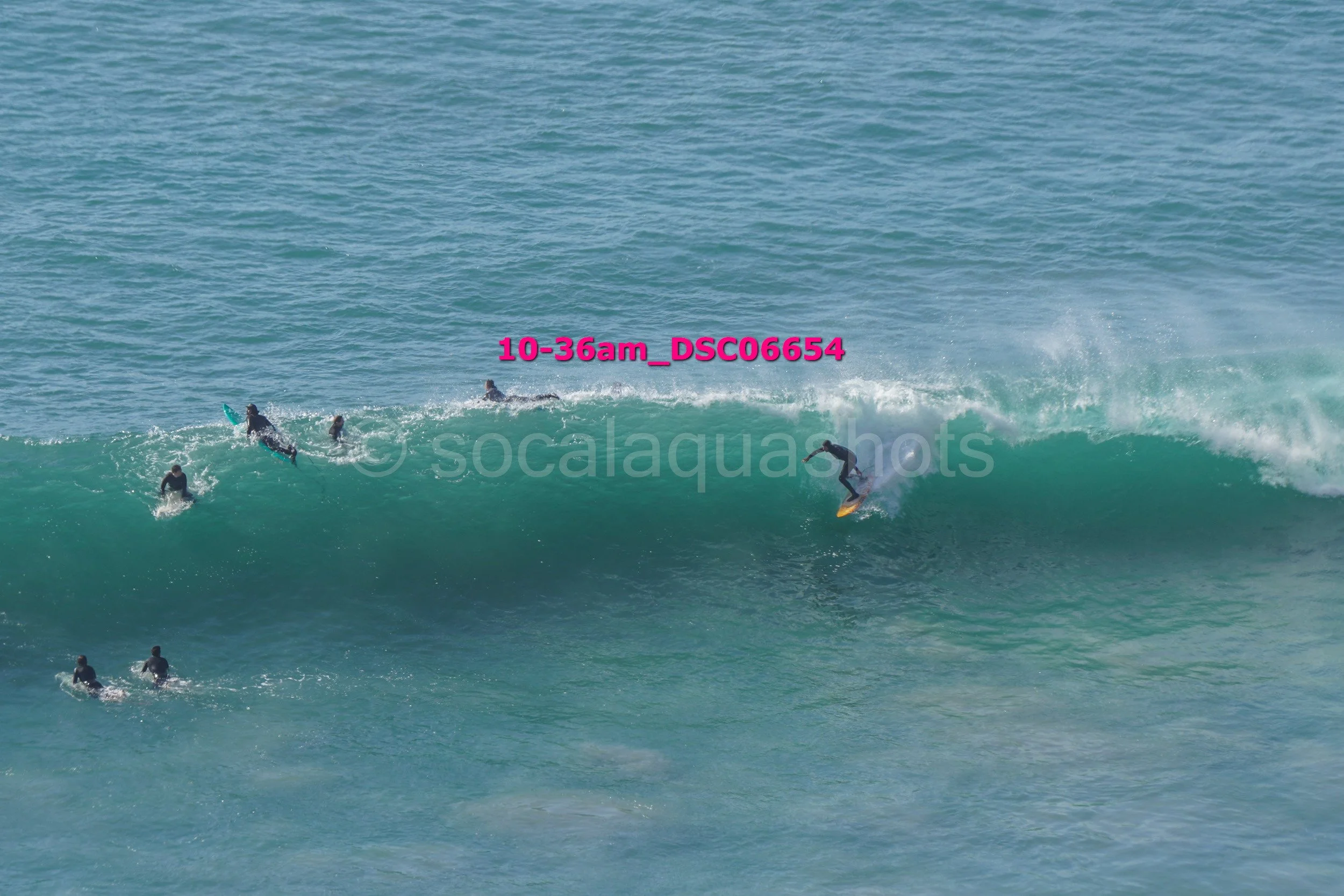 Several surfers in wetsuits riding and waiting on large ocean waves during daytime.