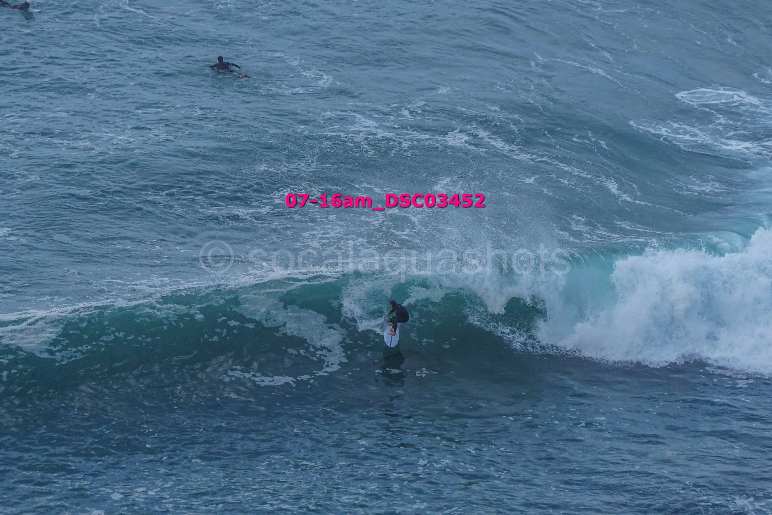 A person surfing on a wave in the ocean with another person swimming in the background.