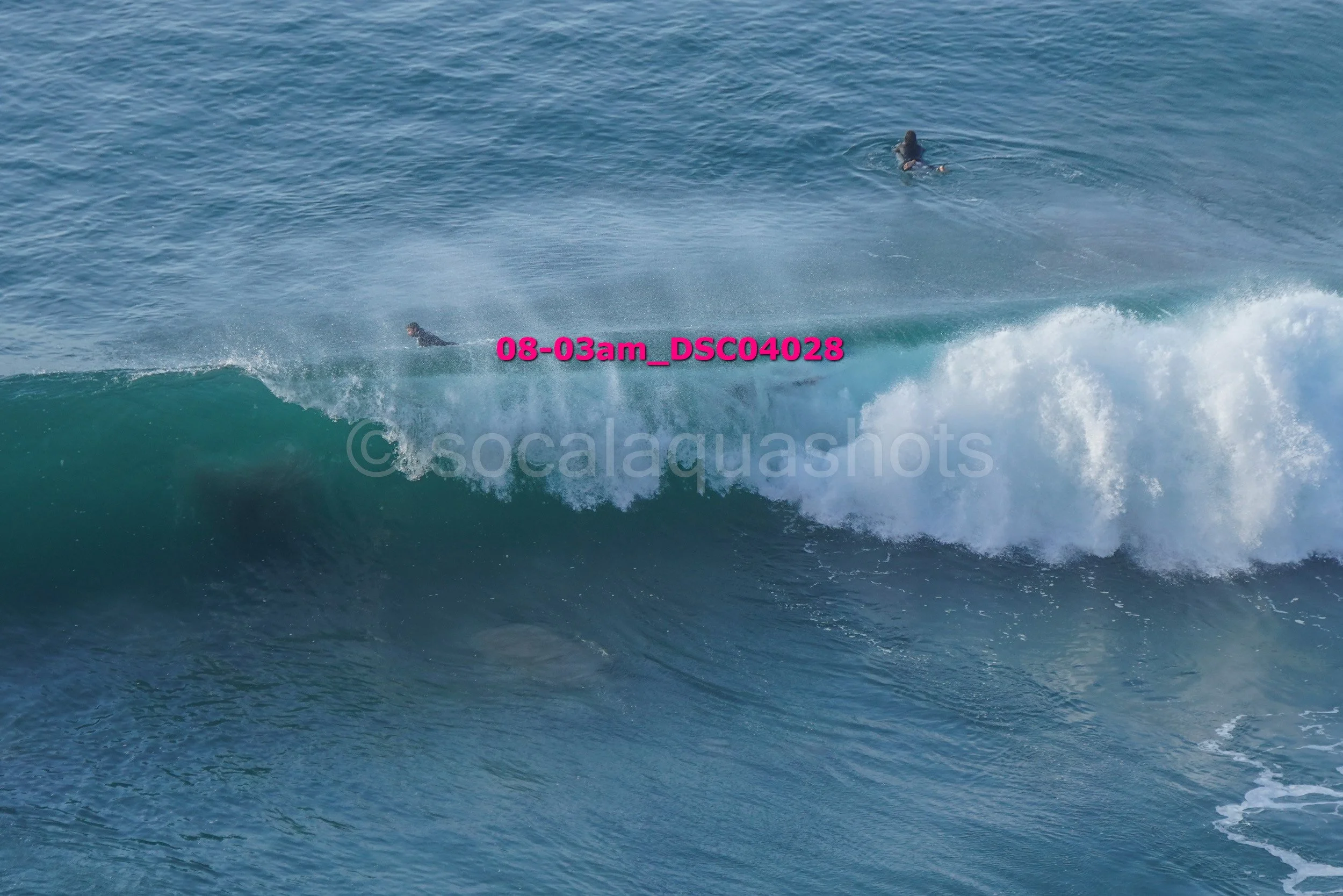 People surfing on large ocean waves, with some surfers riding the wave and others paddling in background.