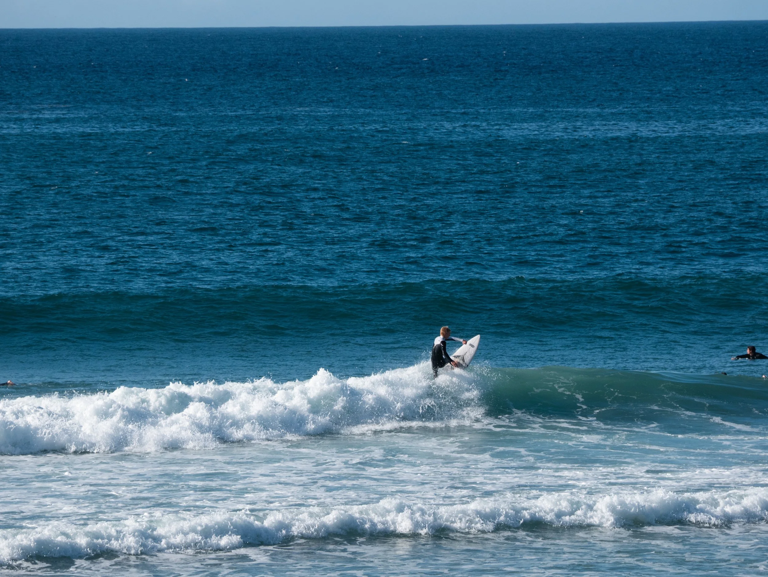 Person surfing on a wave in the ocean with a clear blue sky.