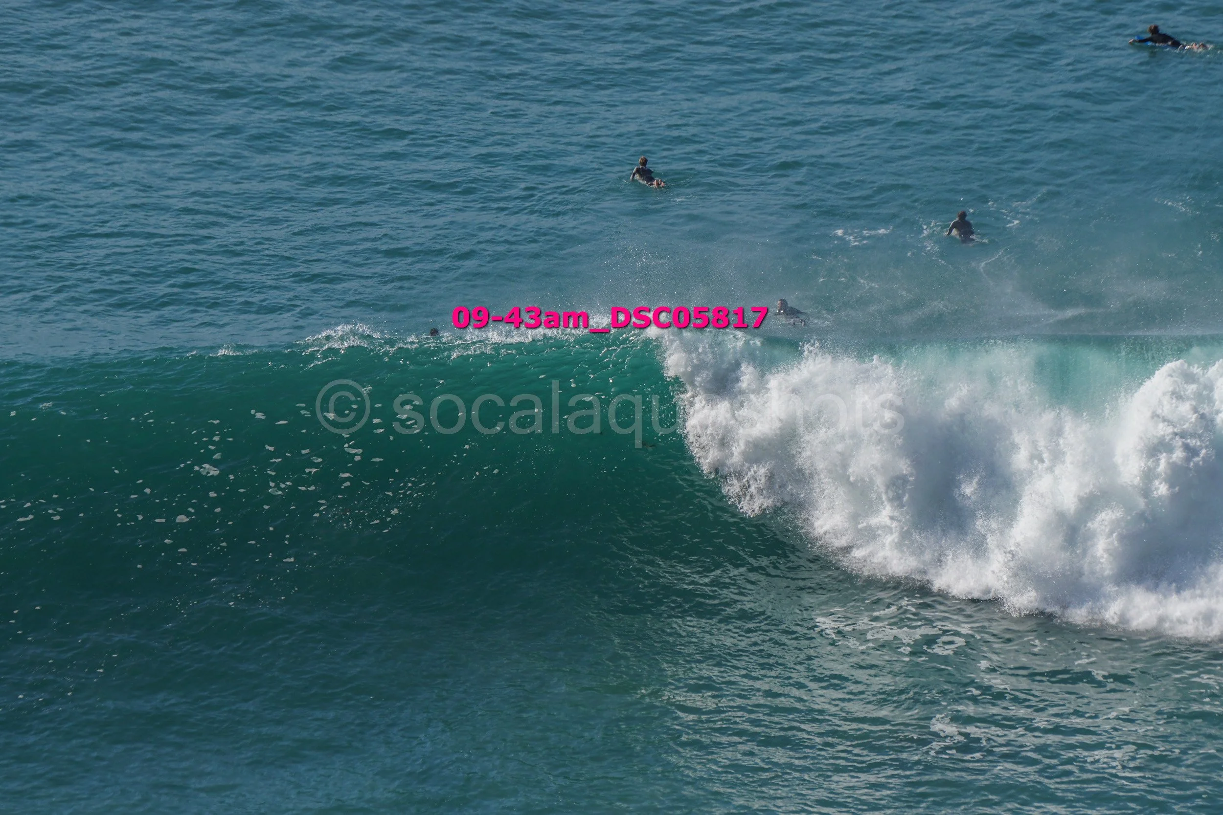 Surfers riding a large wave in the ocean with several others in the water.