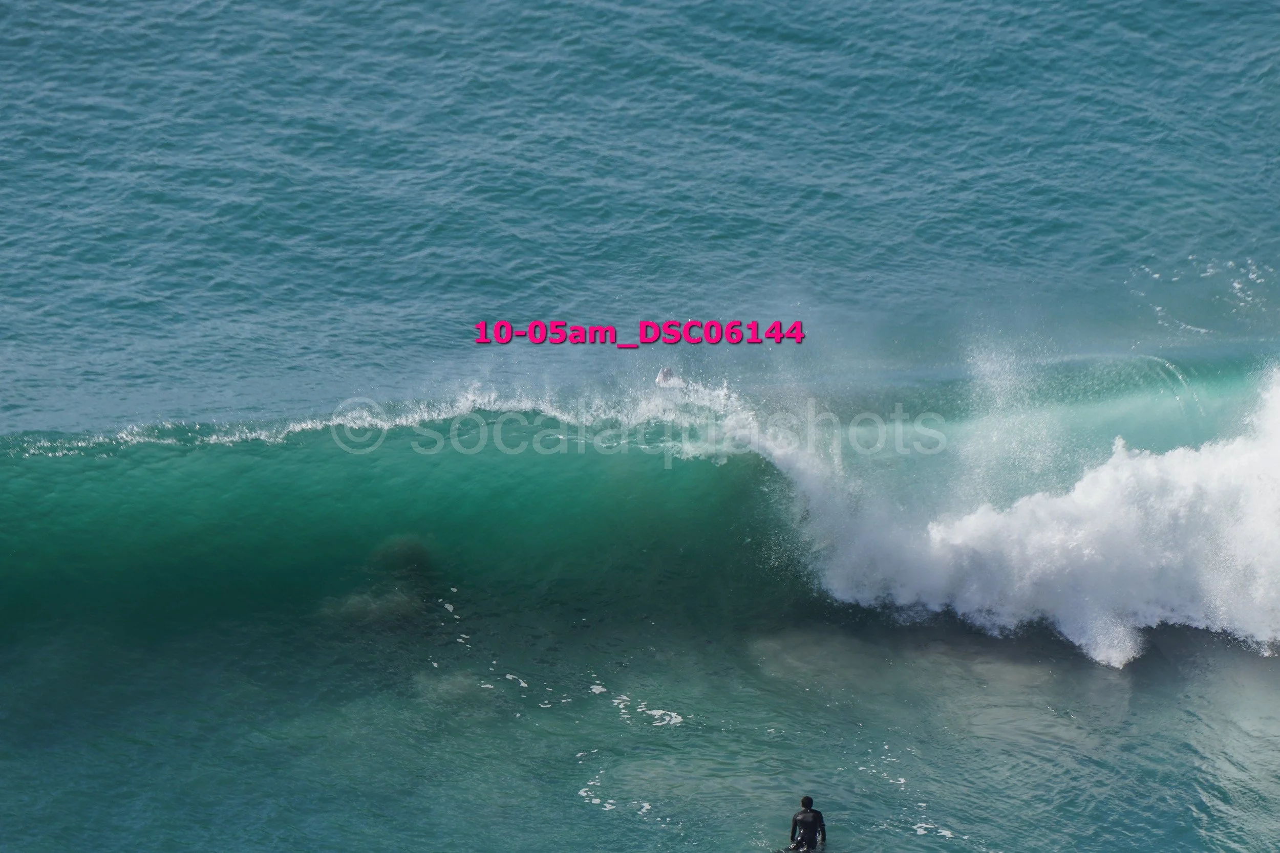 A large ocean wave with a surfer in a wetsuit in front of it.