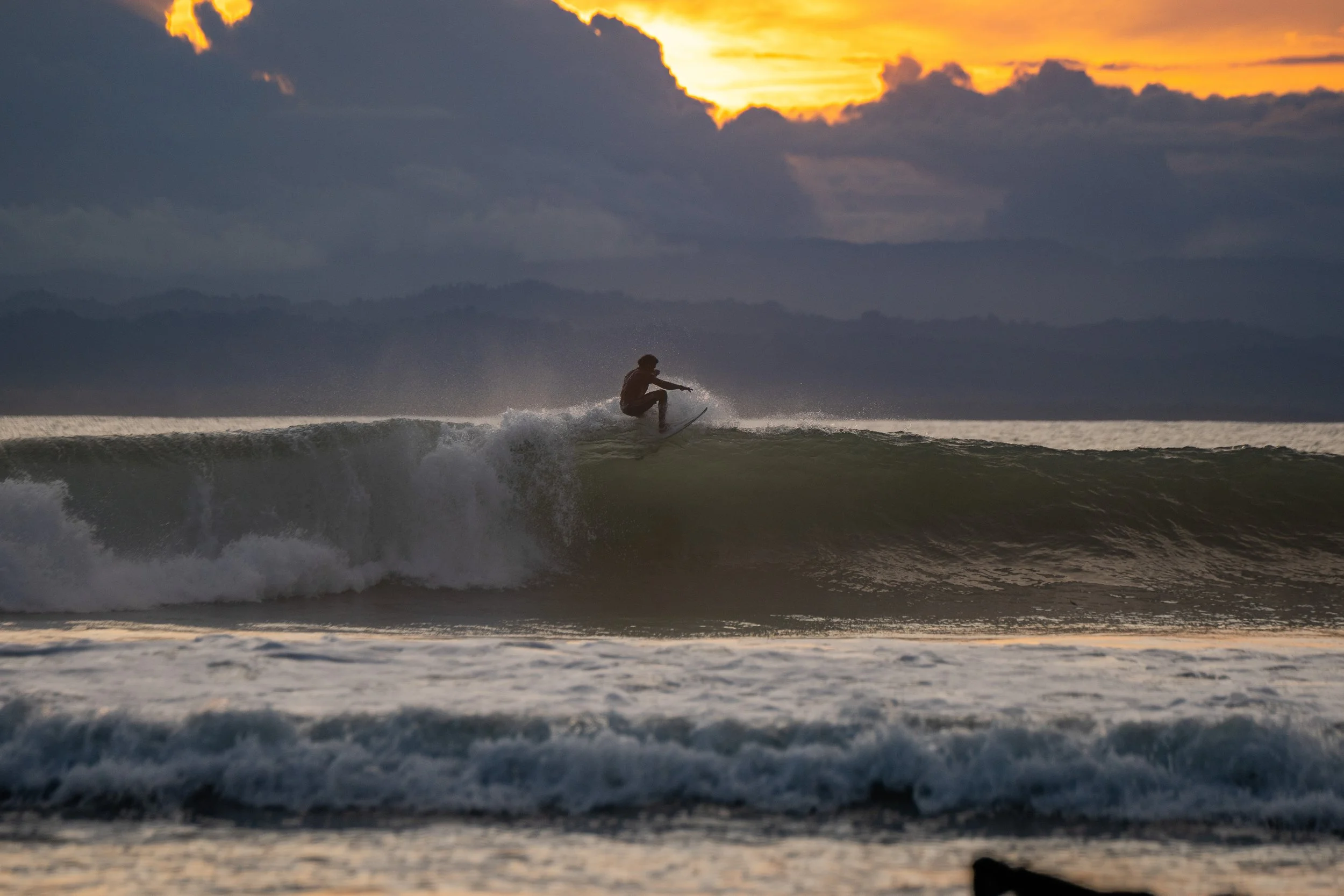 A person surfing on a wave during sunset with a cloudy sky in the background.