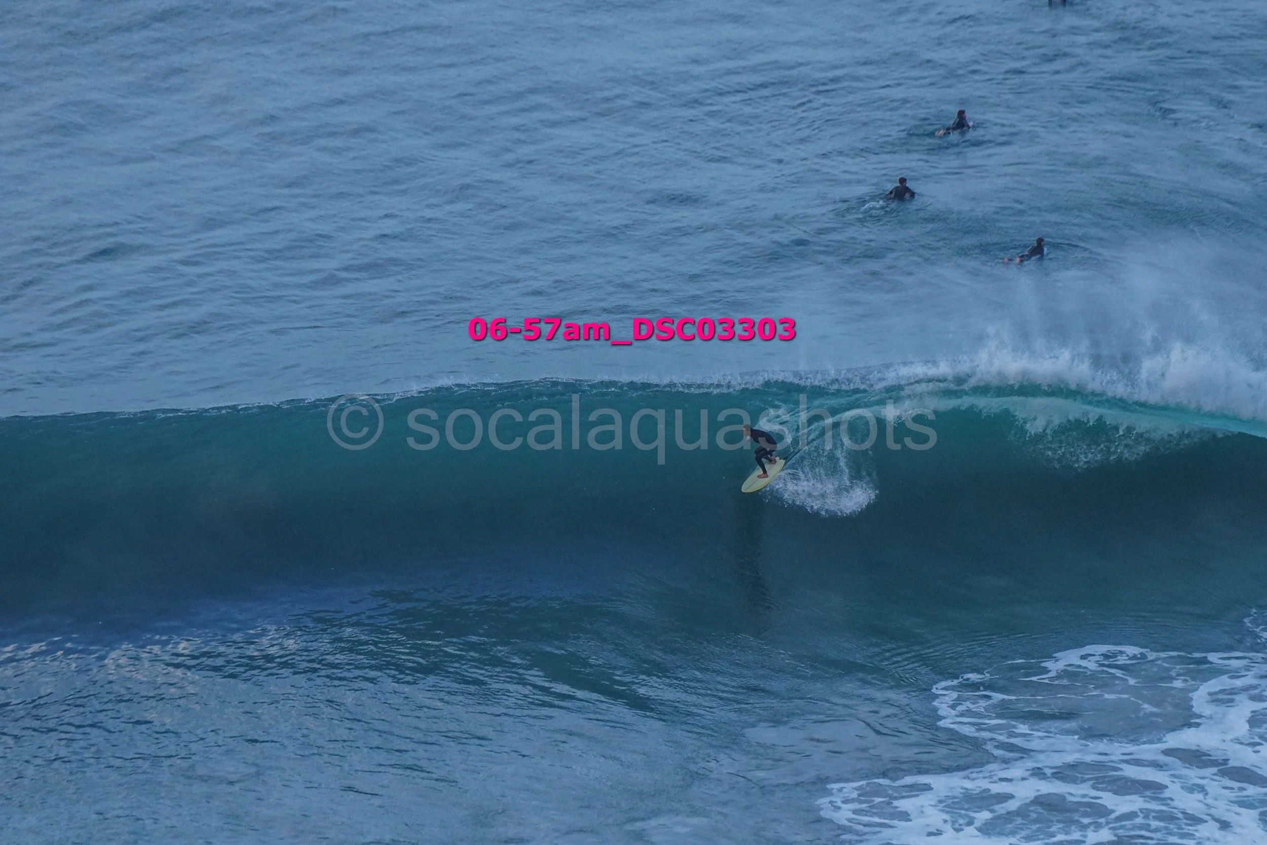 Surfer riding a wave with four people swimming in the water in the background.