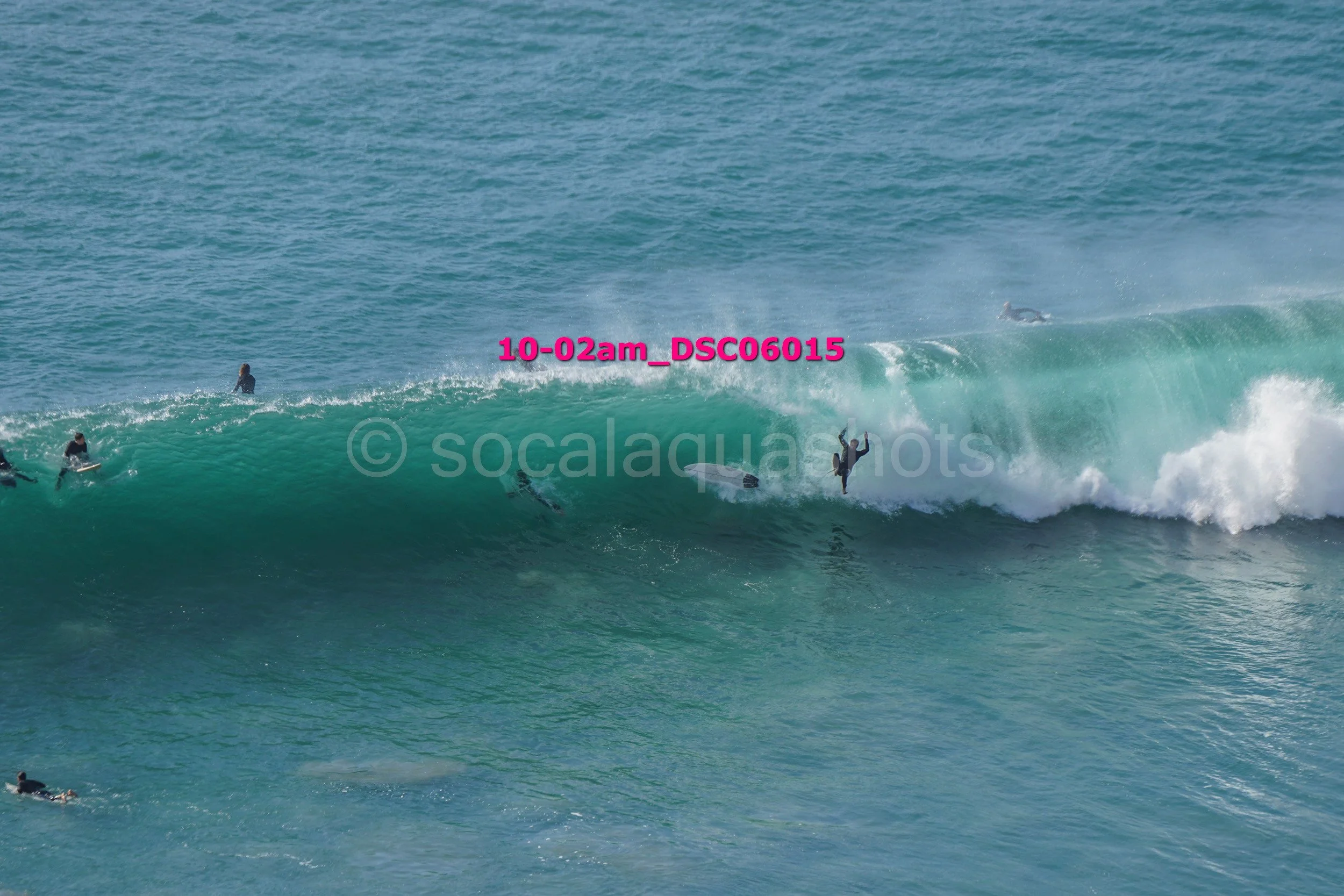 People surfing on large blue ocean waves, with some surfers riding or falling off their boards.