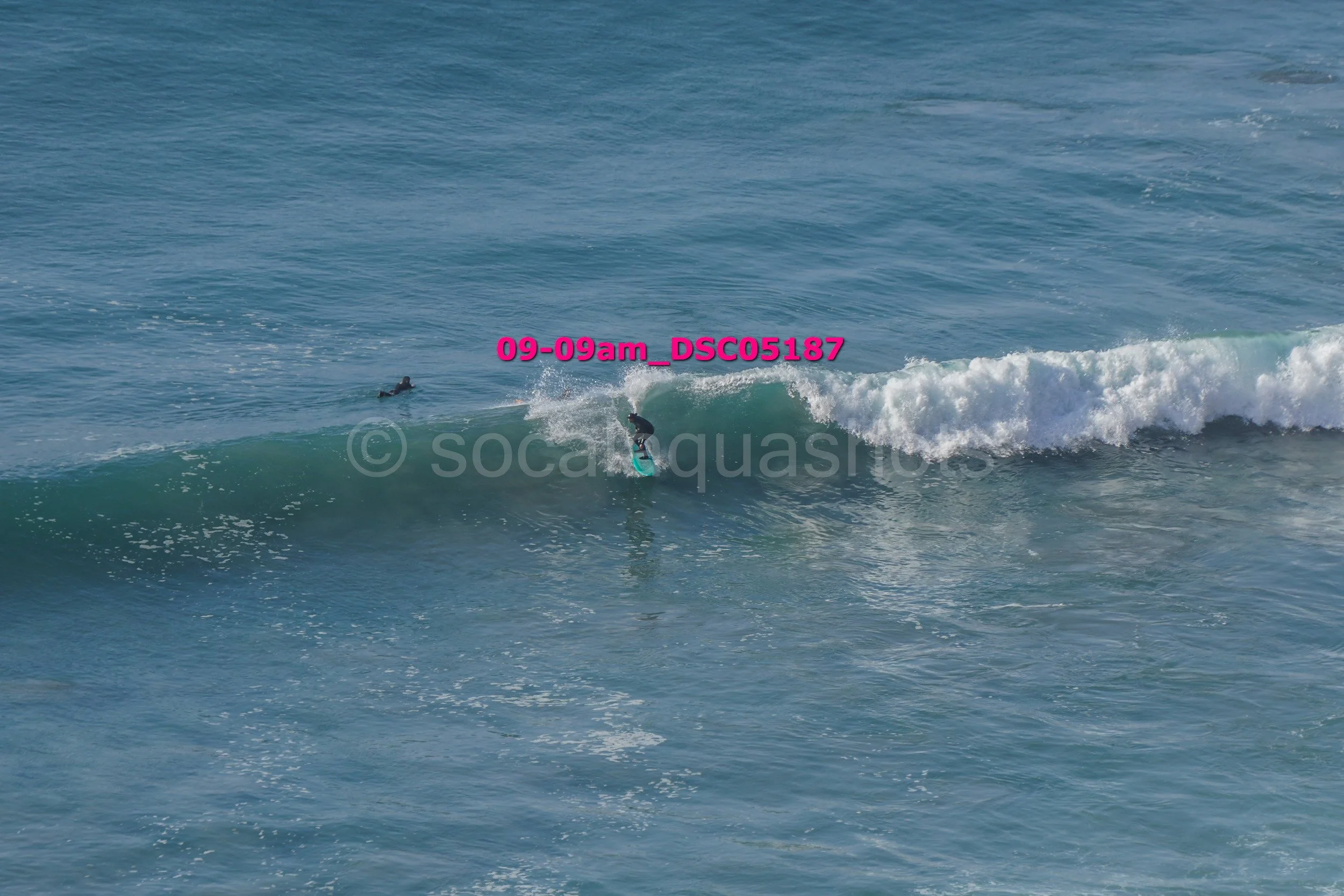 A person surfing on a wave in the ocean with another person in the water nearby.