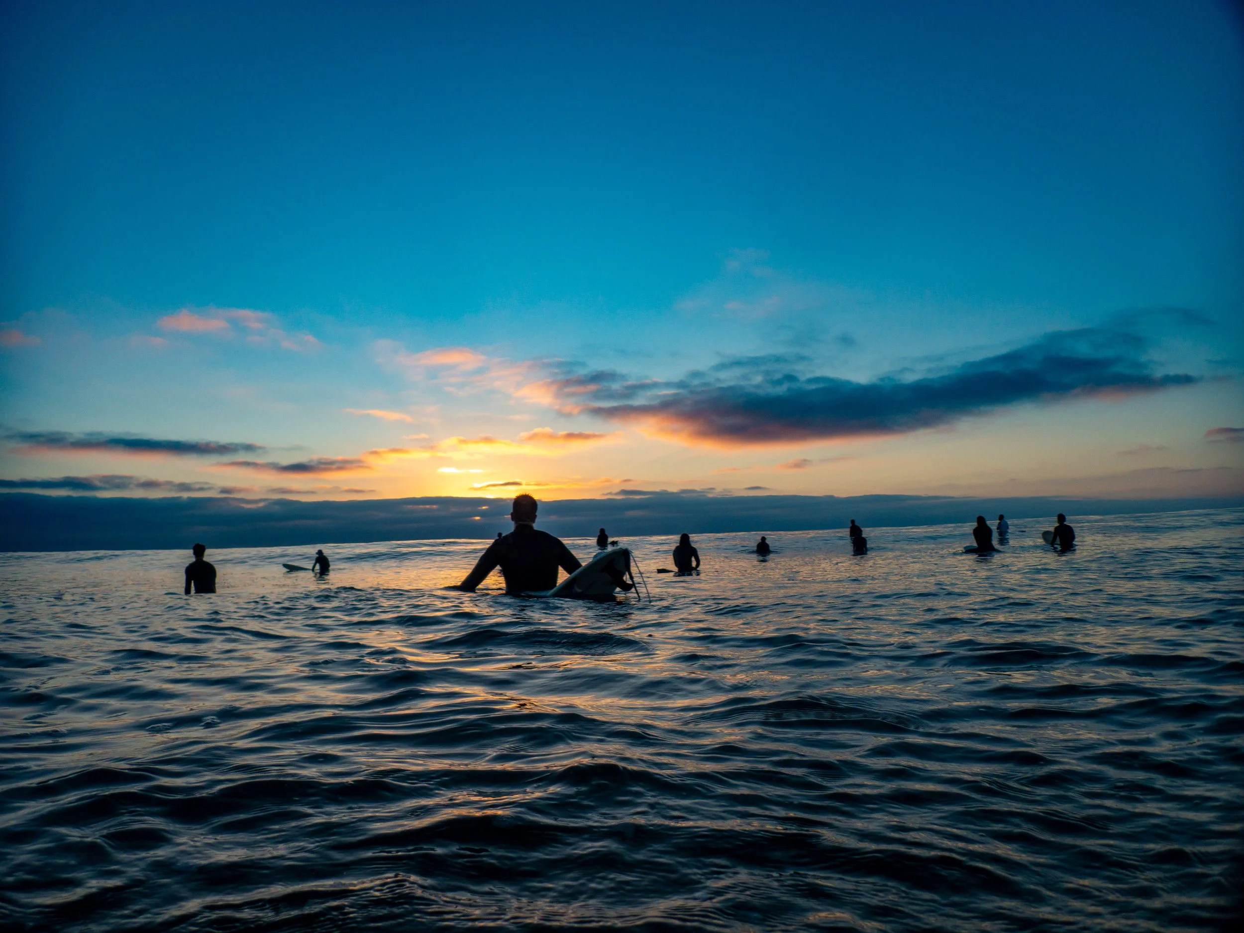 Surfers waiting in the ocean during sunset.