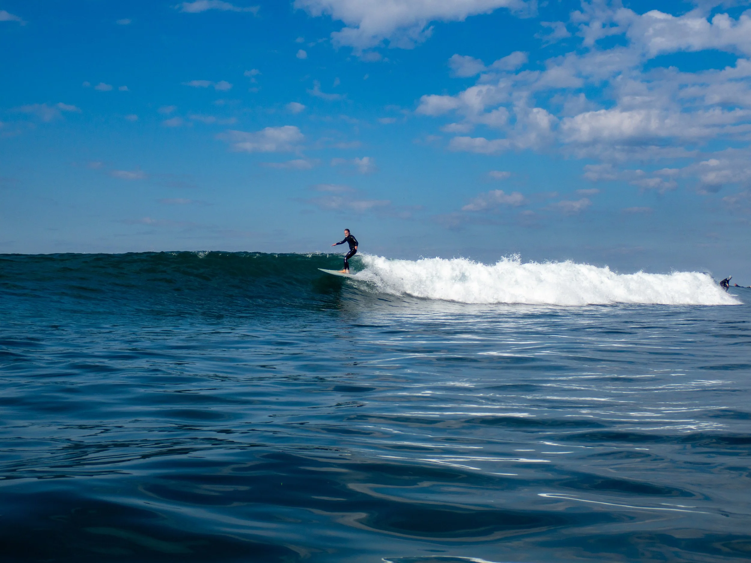 A person surfing on a wave in the ocean under a partly cloudy sky.
