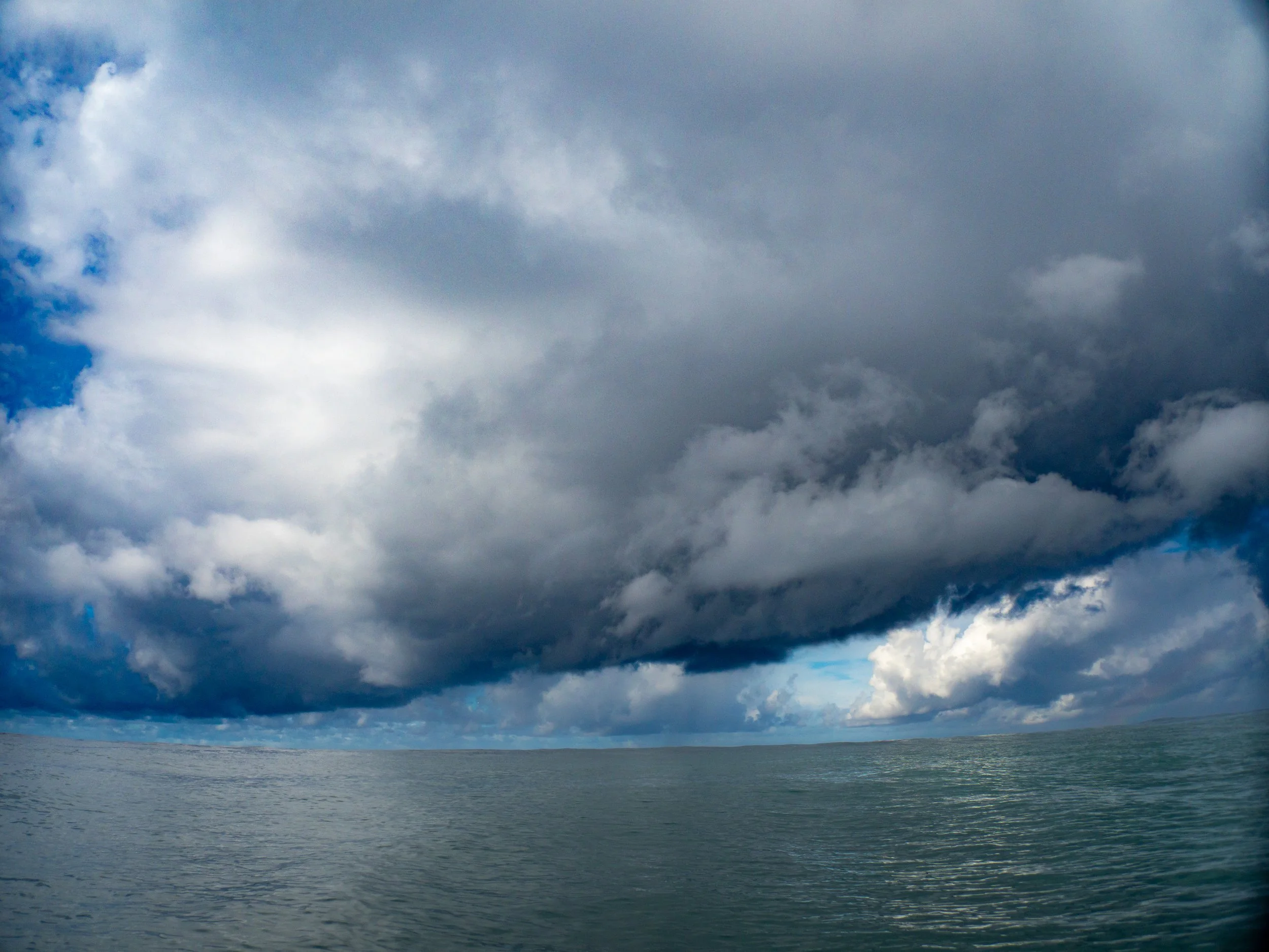 A large body of water with a cloudy sky overhead, with dark clouds and some patches of blue sky.