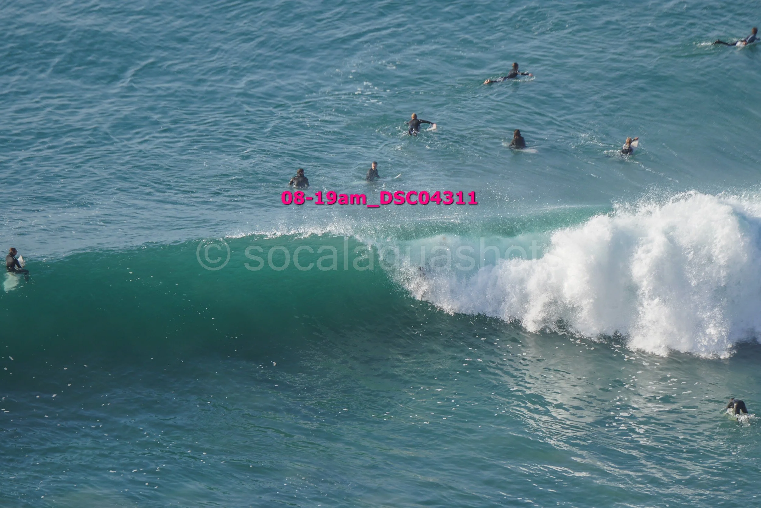 Multiple surfers riding and waiting on surfboards in the ocean waves during daytime.