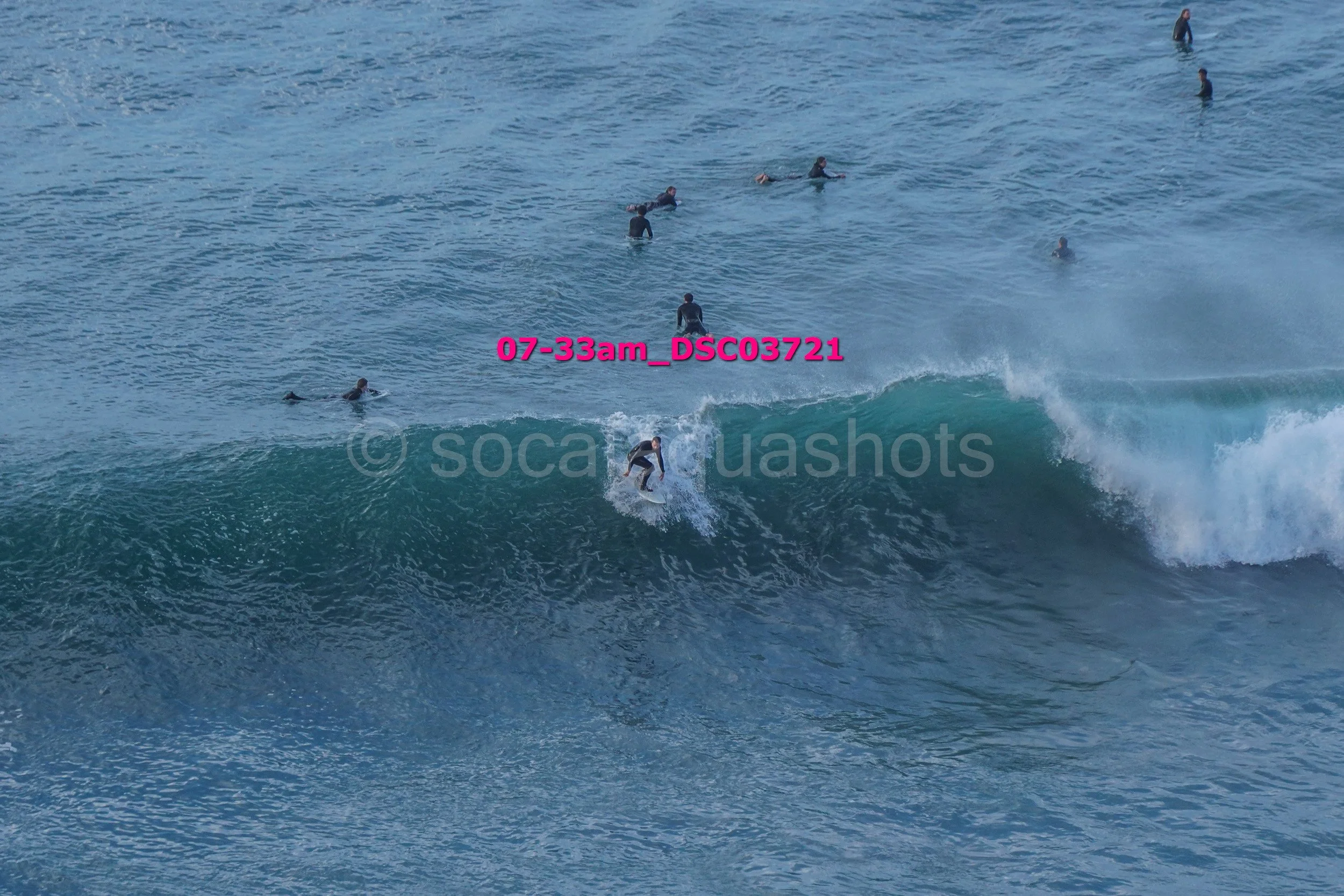 A person surfing on a wave with several other swimmers in the ocean in the background.