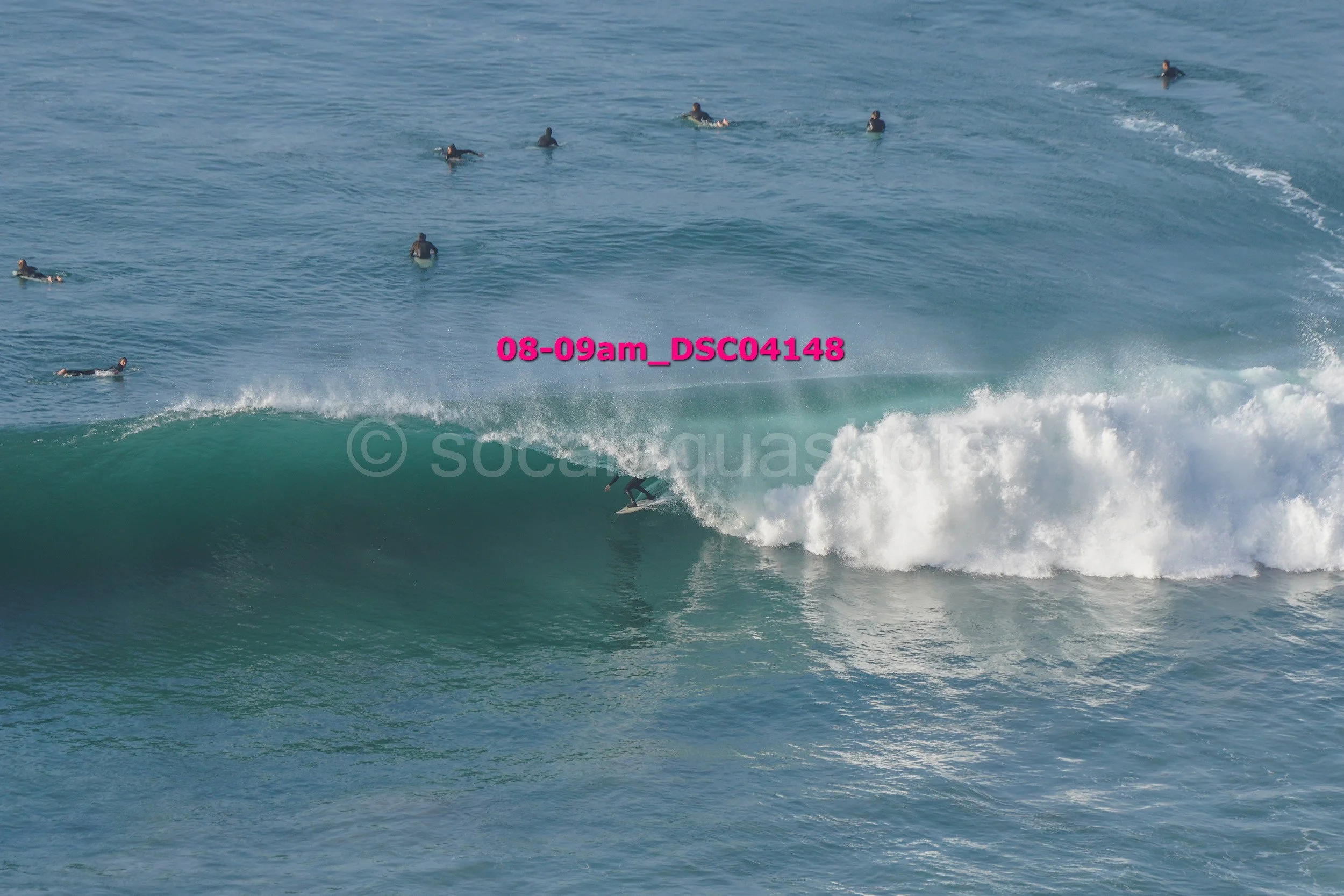 A surfer riding inside a large breaking wave while several surfers float in the water in the background.