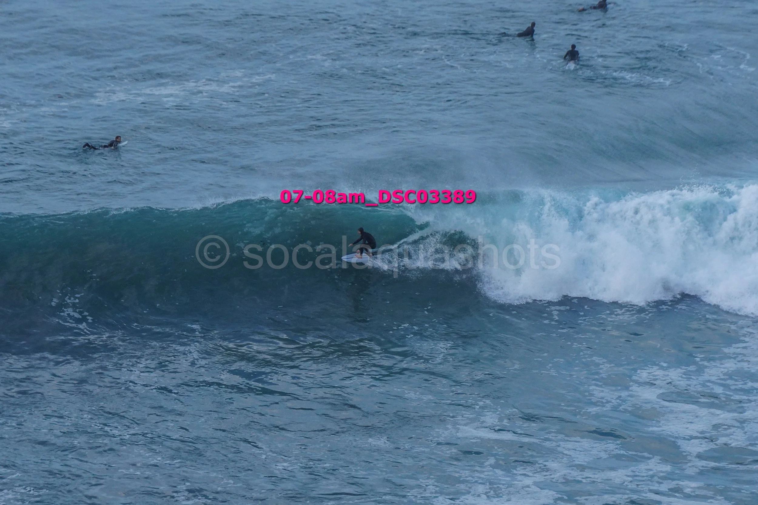 A person surfing on a wave in the ocean with several other swimmers in the background.