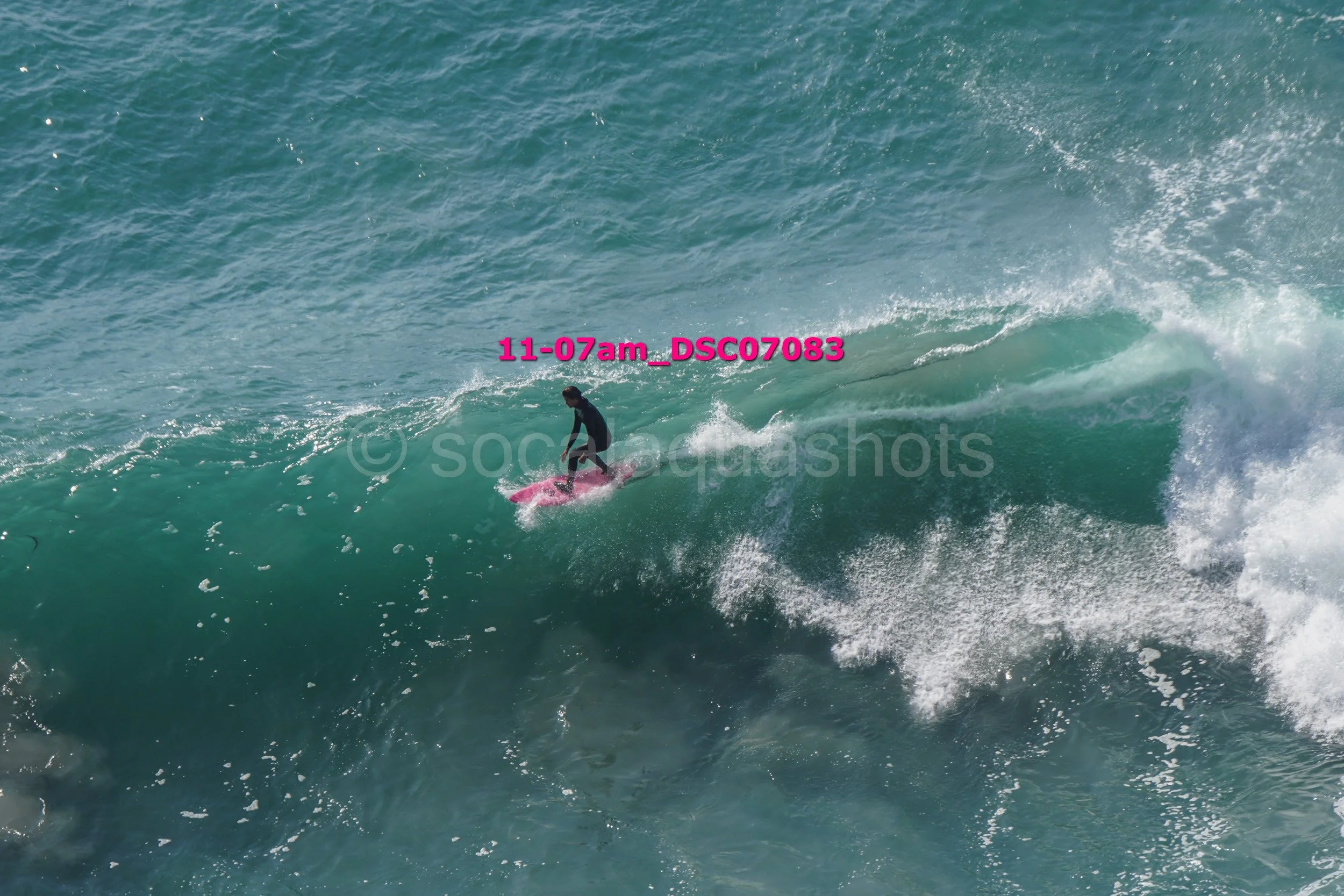 A person surfing on a pink surfboard riding a large ocean wave with white foam