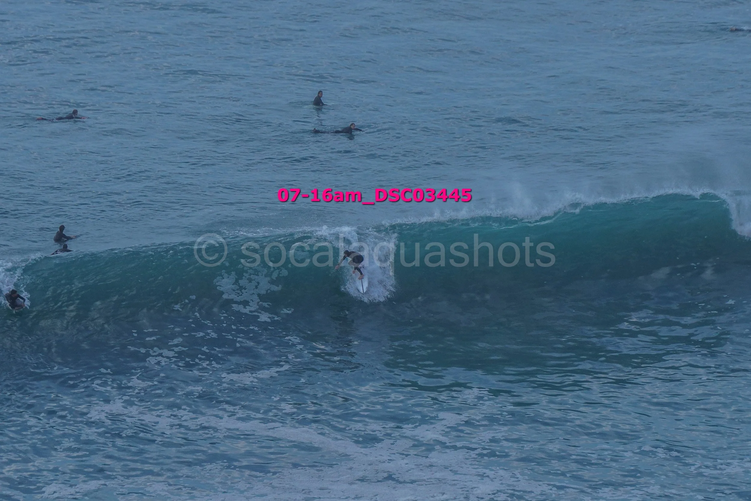 A person surfing on a wave with several people in the water watching.