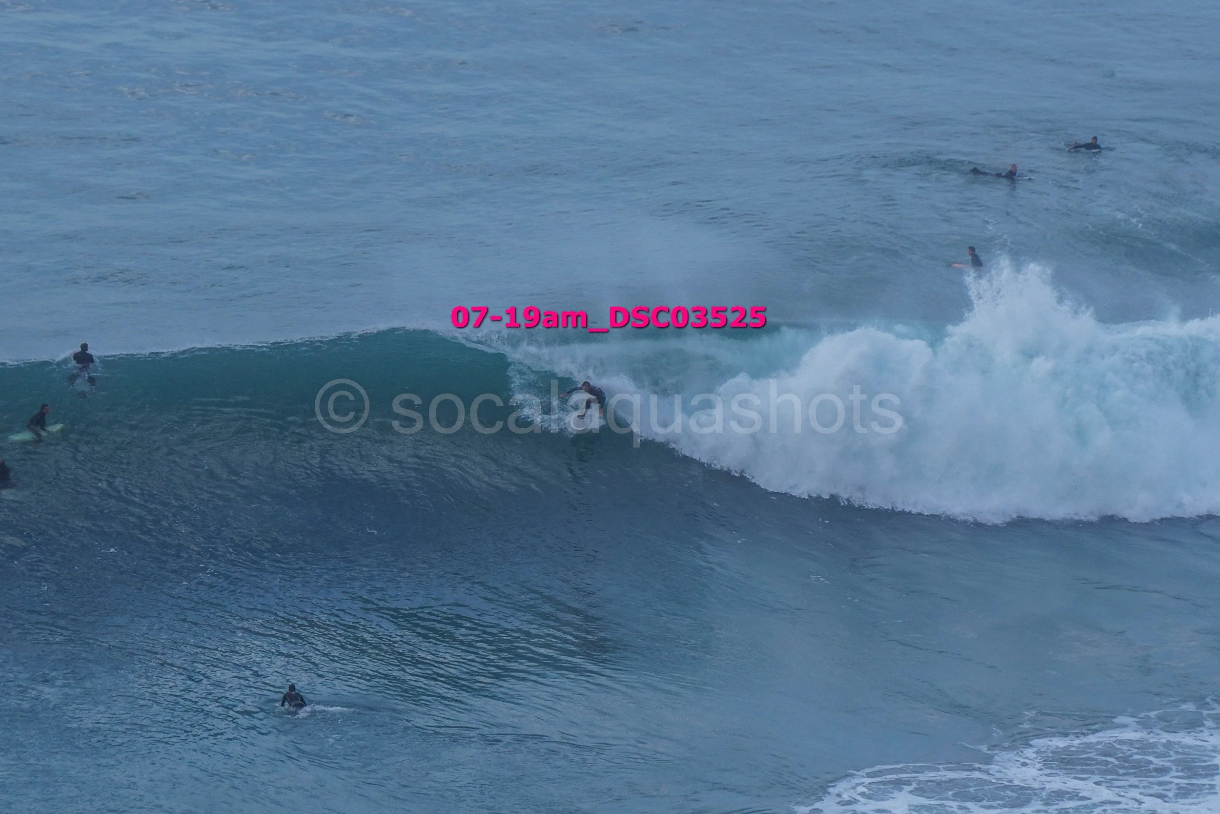 Surfer riding a wave with several surfers in the water around him.