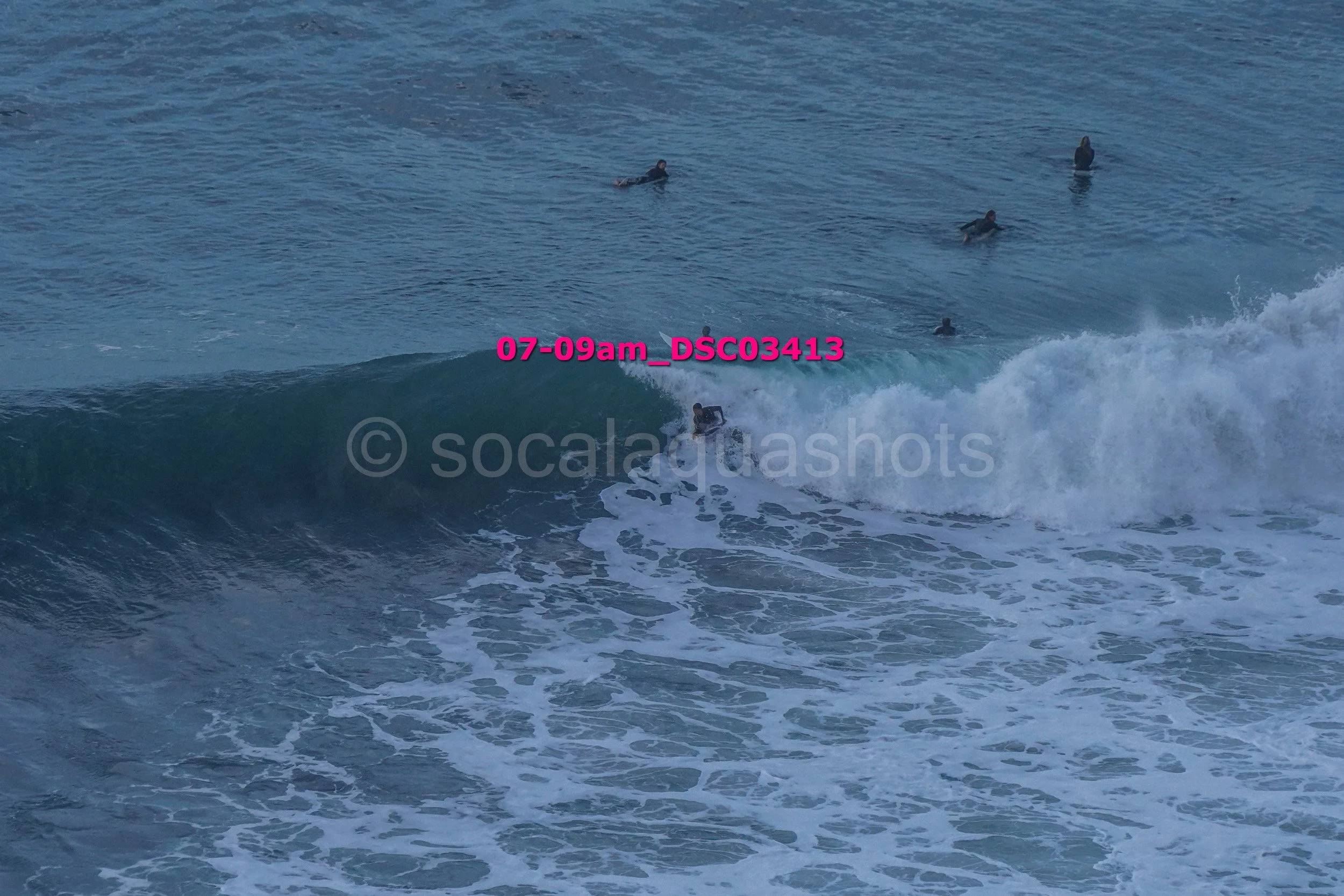 A person surfing on a wave with multiple people swimming in the water nearby.