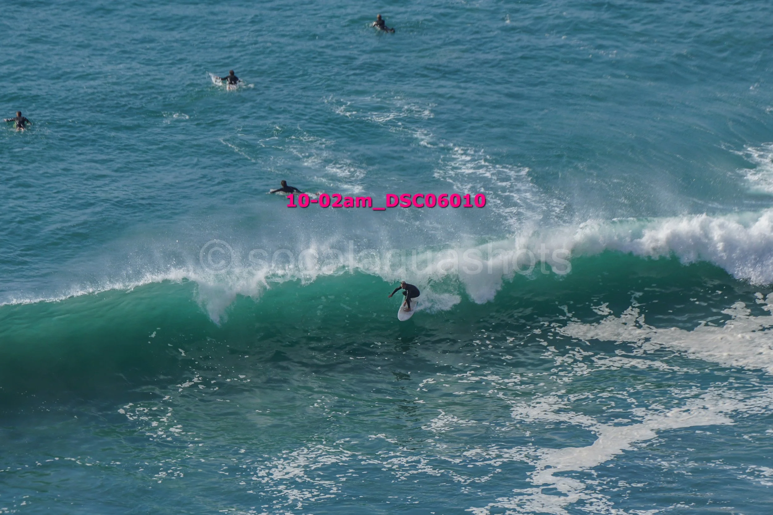 Surfer riding a wave while other surfers wait in the water.