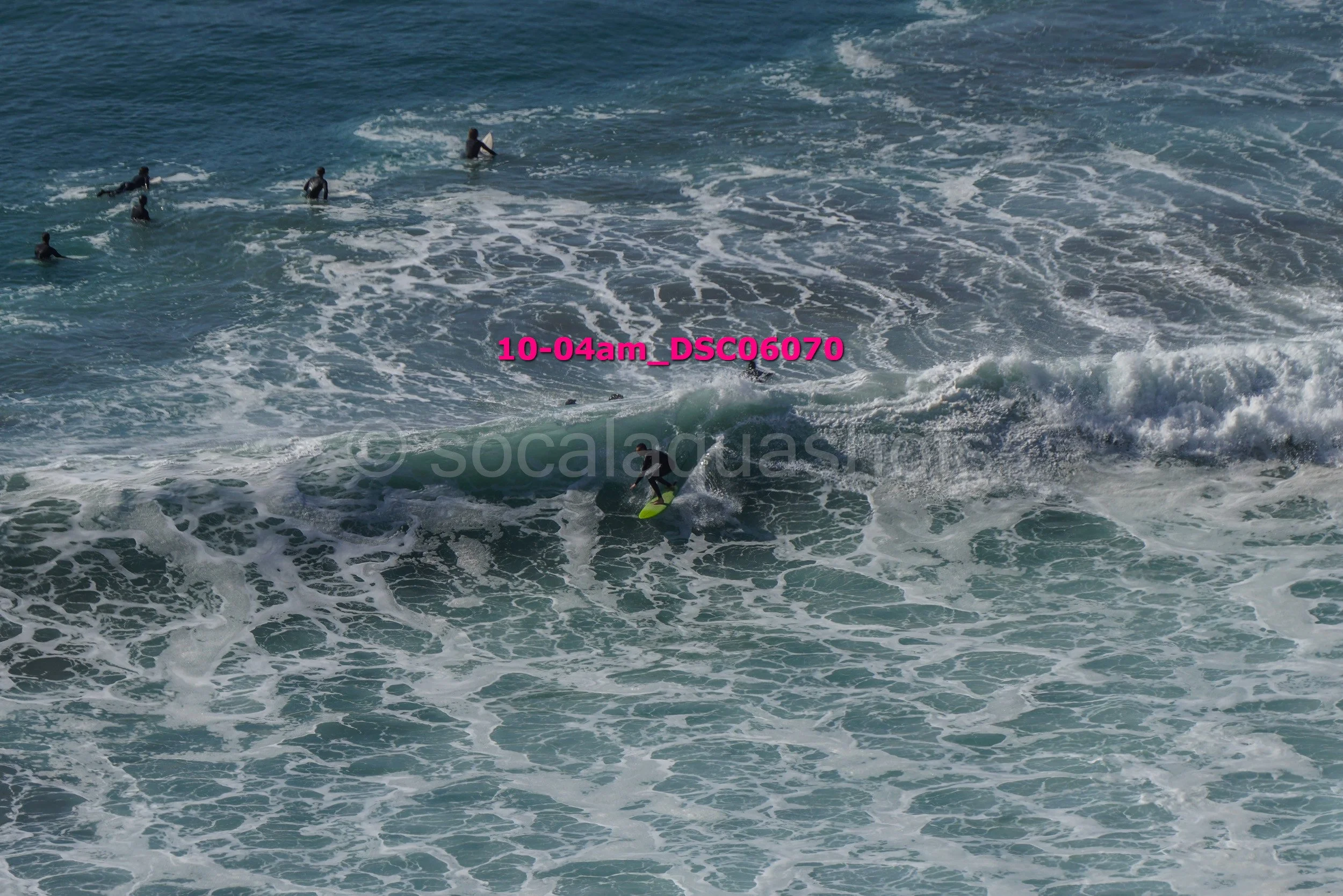 Multiple surfers in the ocean, some riding waves, others waiting or swimming.