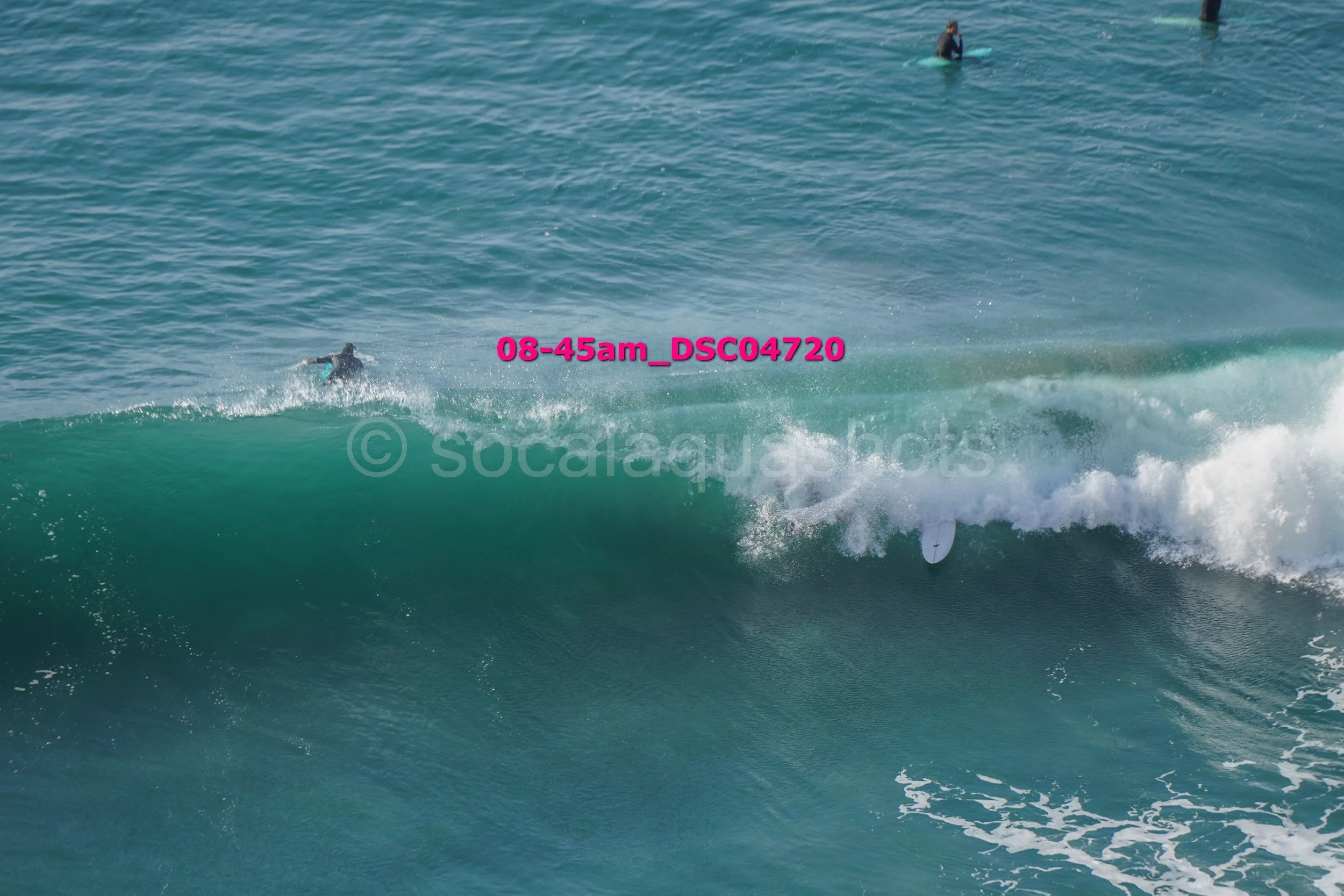 A person surfing a wave in the ocean, with two other surfers visible in the water in the background.