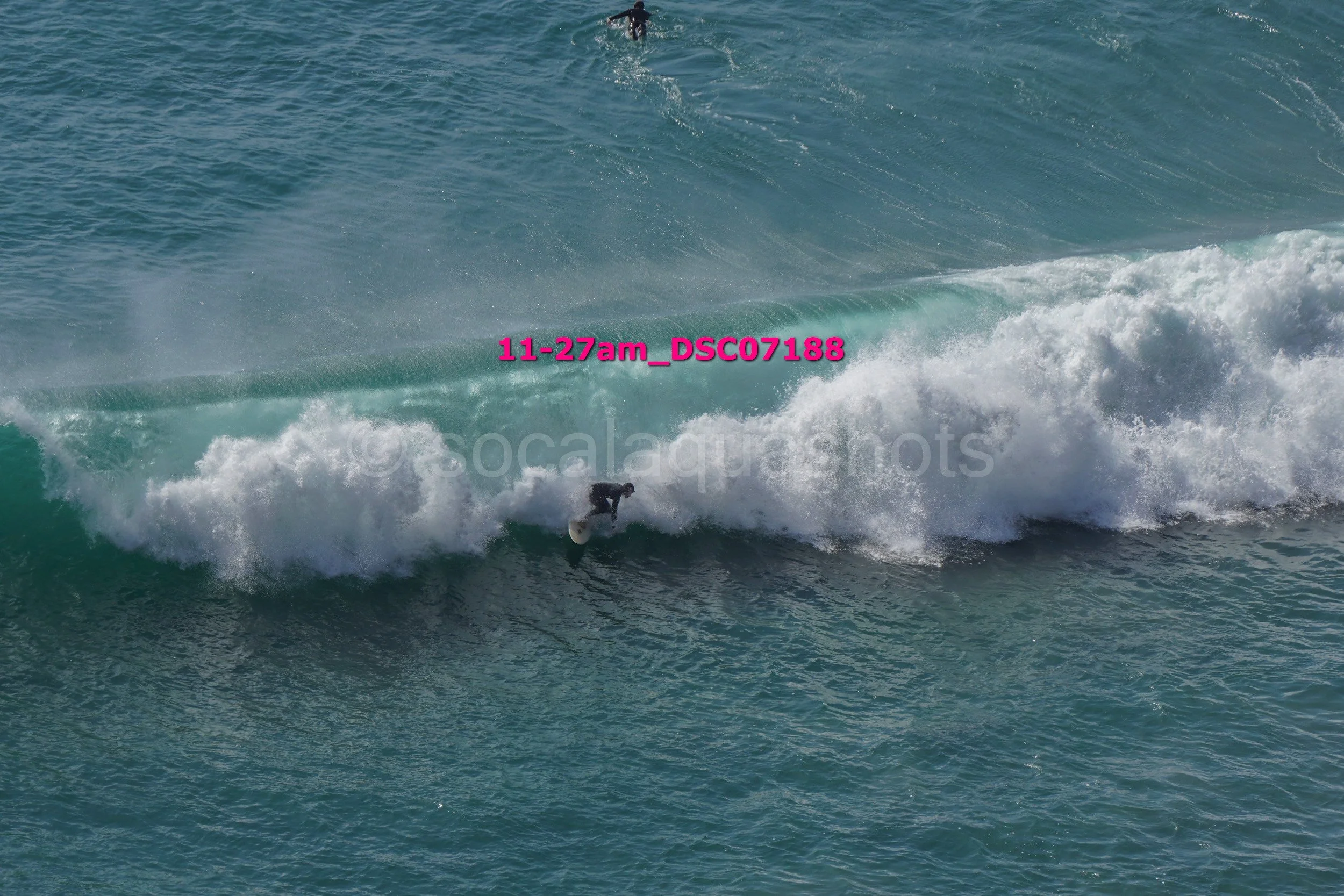 Surfer riding a wave in the ocean, with another surfer visible in the distance.