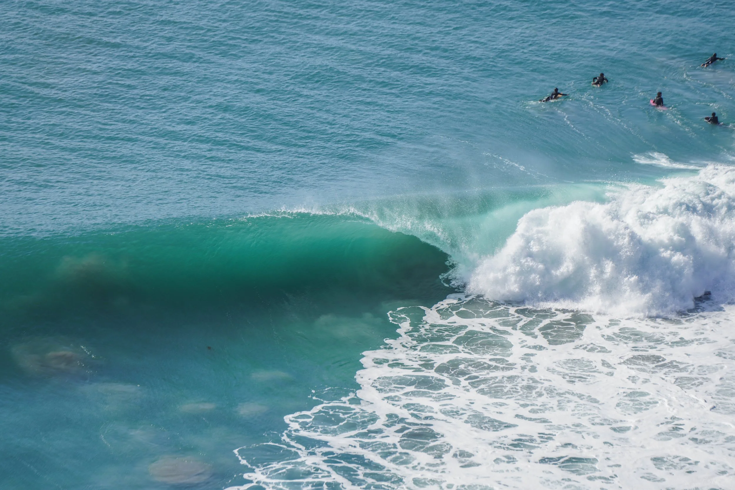 A large ocean wave with a group of surfers riding the wave in the background.