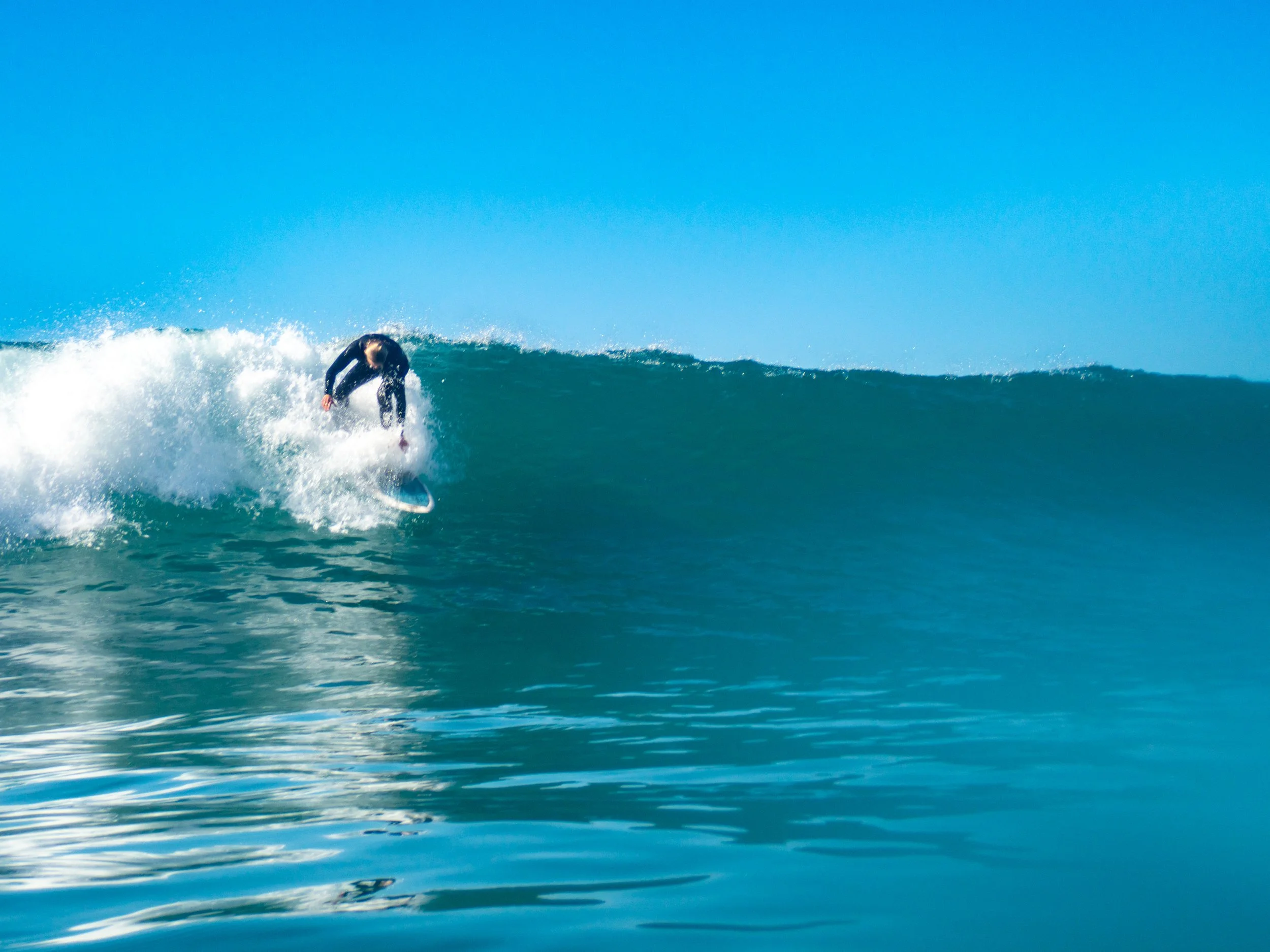 A person surfing on a wave in the ocean under a clear blue sky.